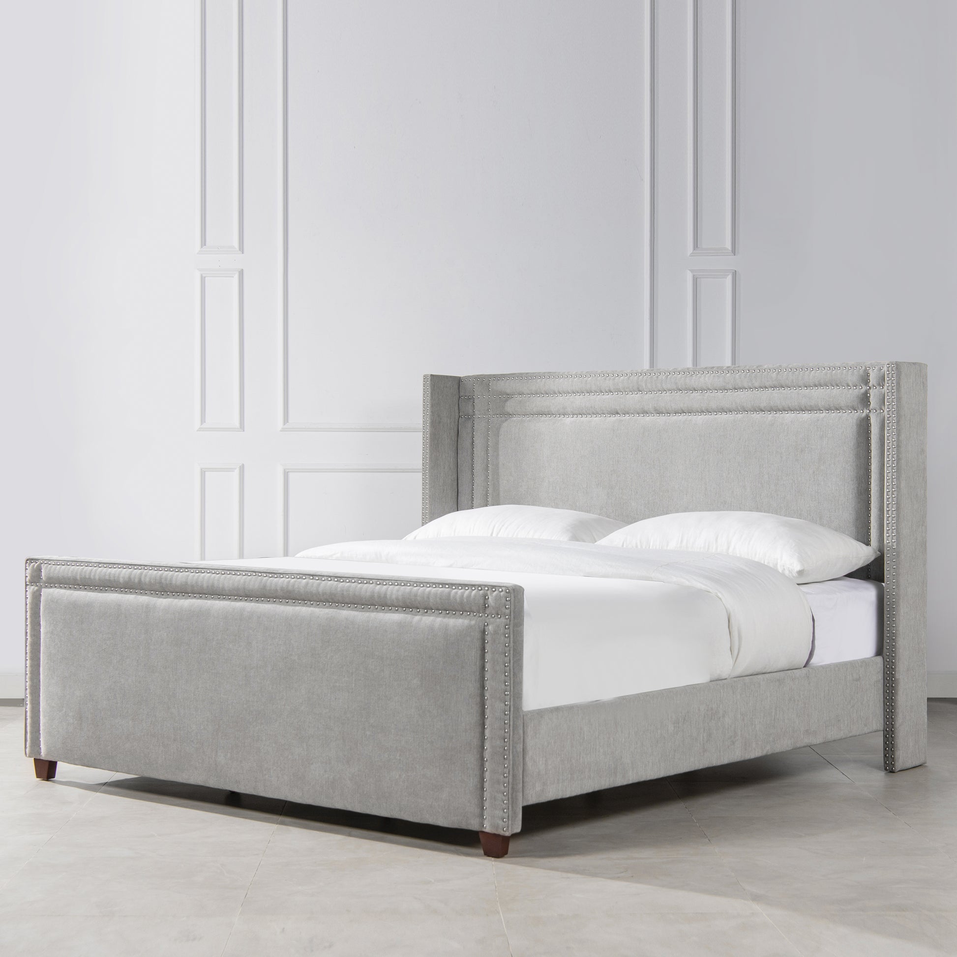 Gray fabric wingback bed with silver nailhead trim and white bedding
