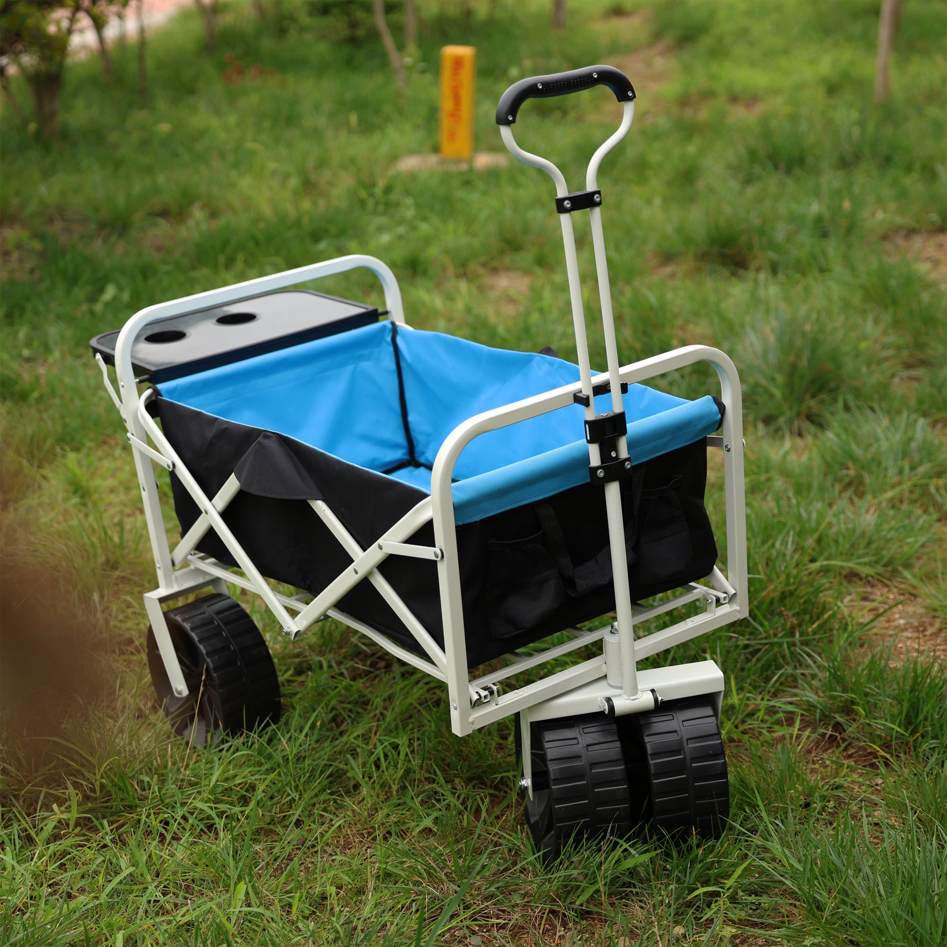 Blue and black foldable wagon with cup holders on a grassy background