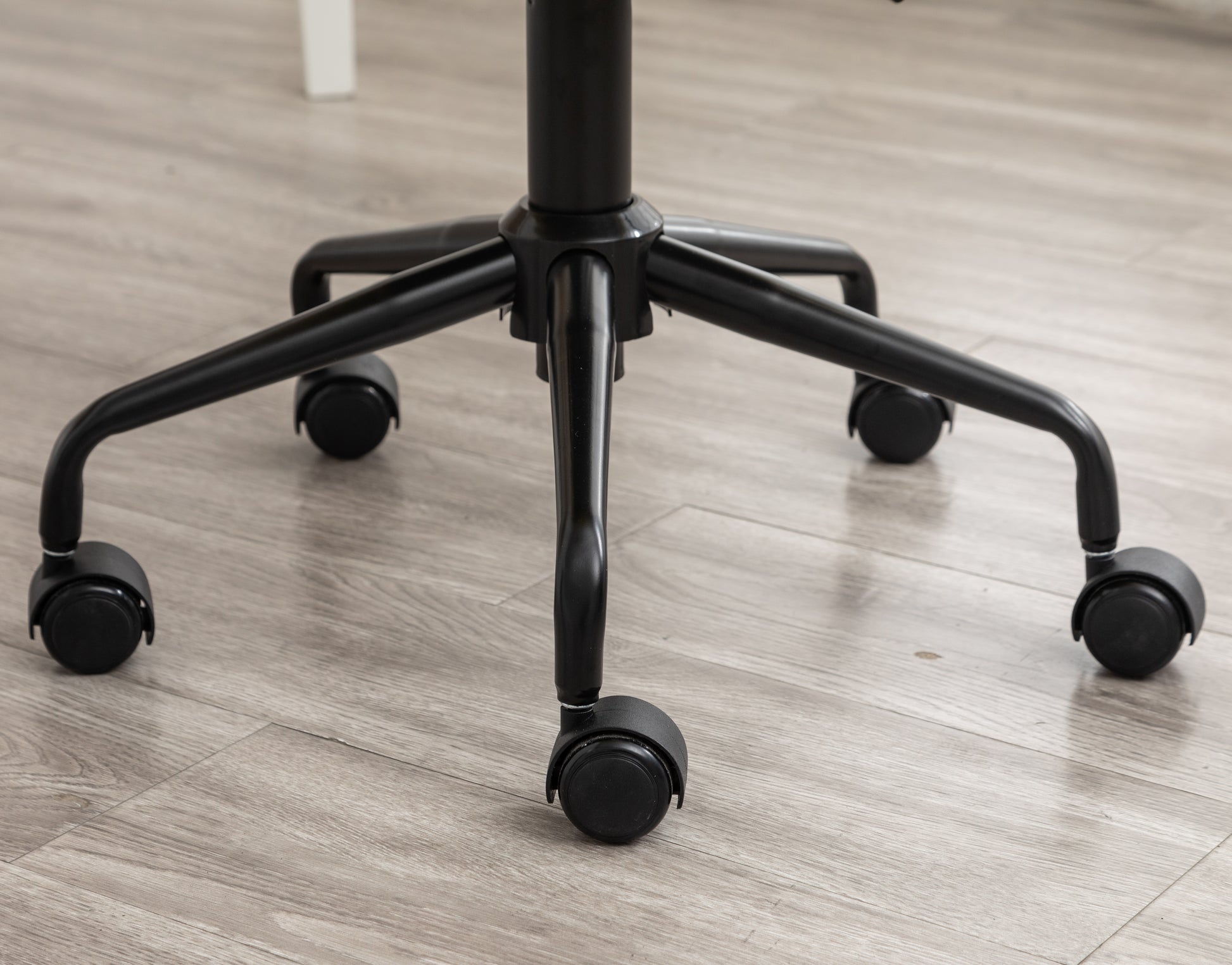 Black metal office chair base with five rolling casters on a woodeffect floor