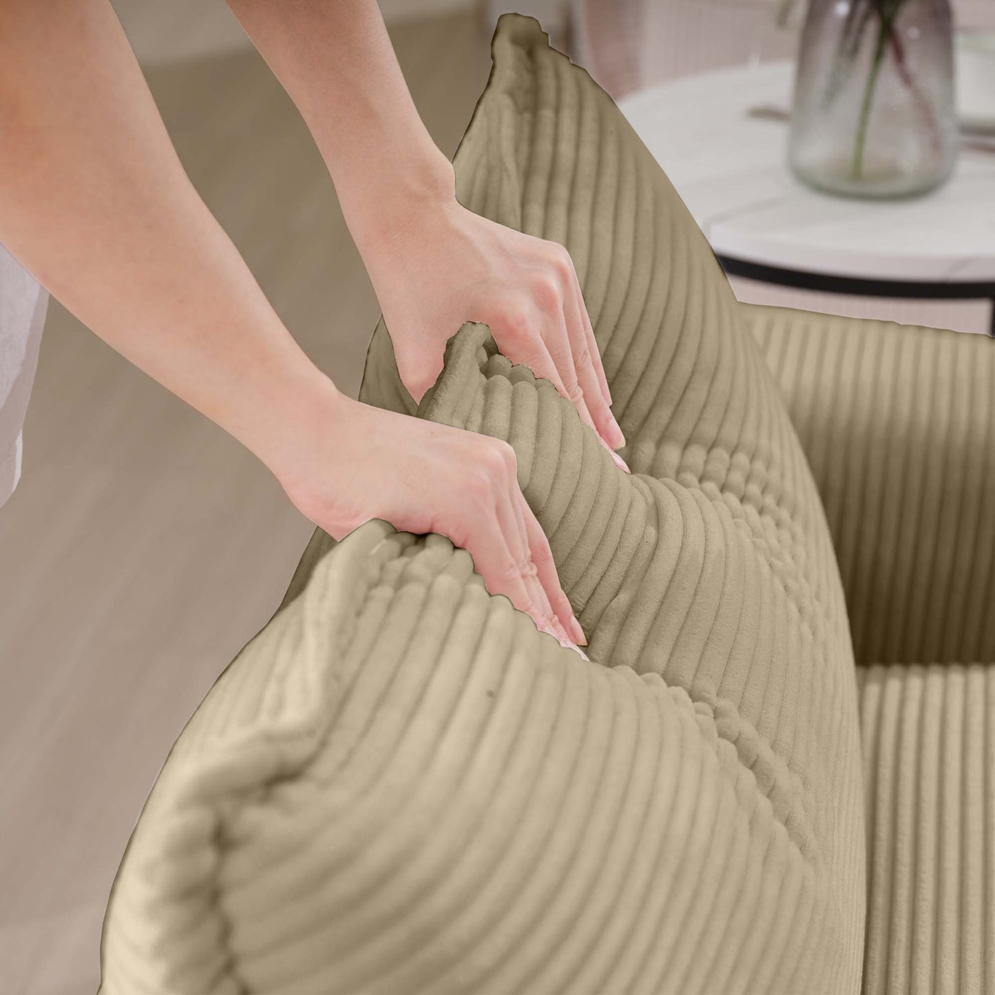 Closeup of hands adjusting a plush beige corduroy cushion for sofa comfort