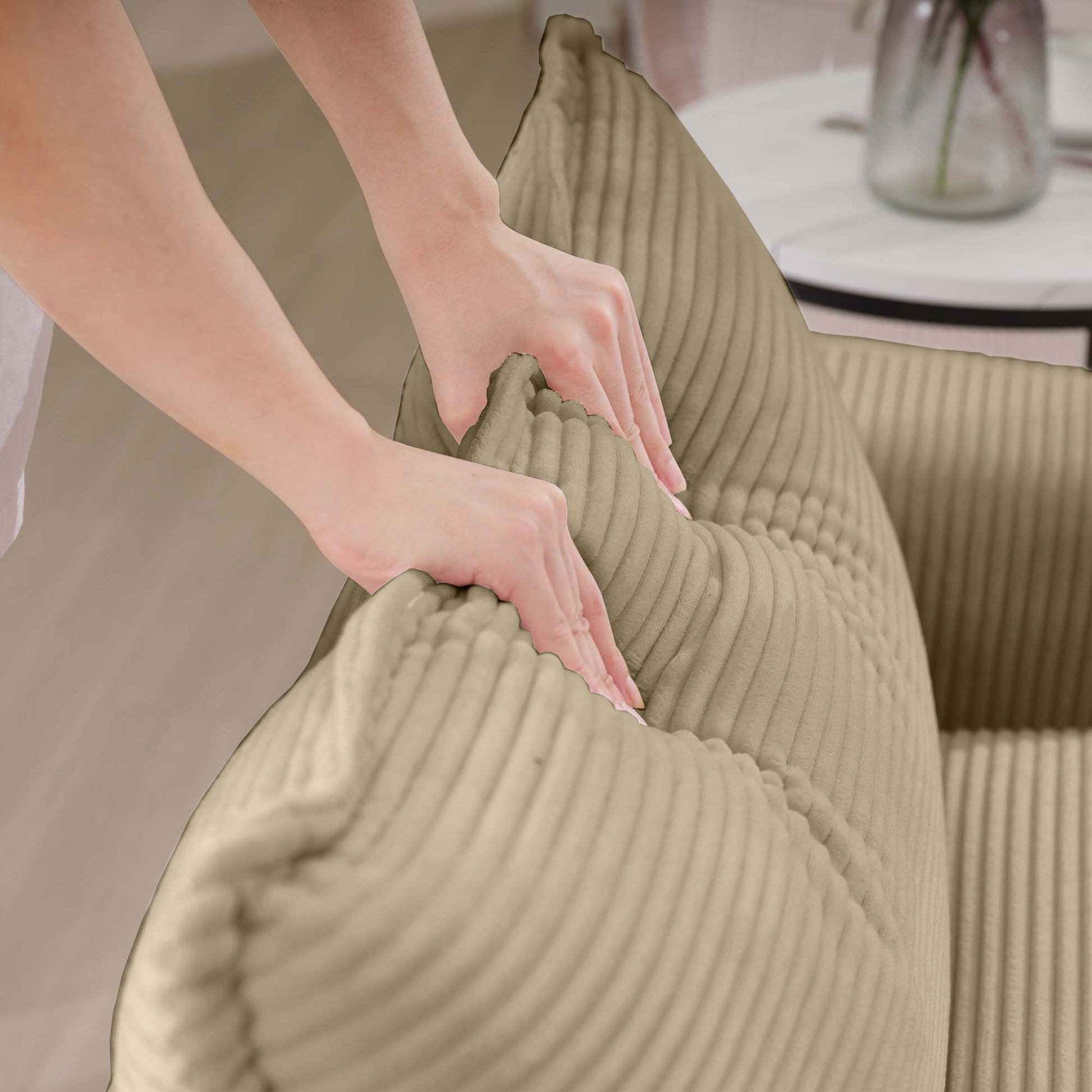 Closeup of hands adjusting a plush beige corduroy cushion for sofa comfort