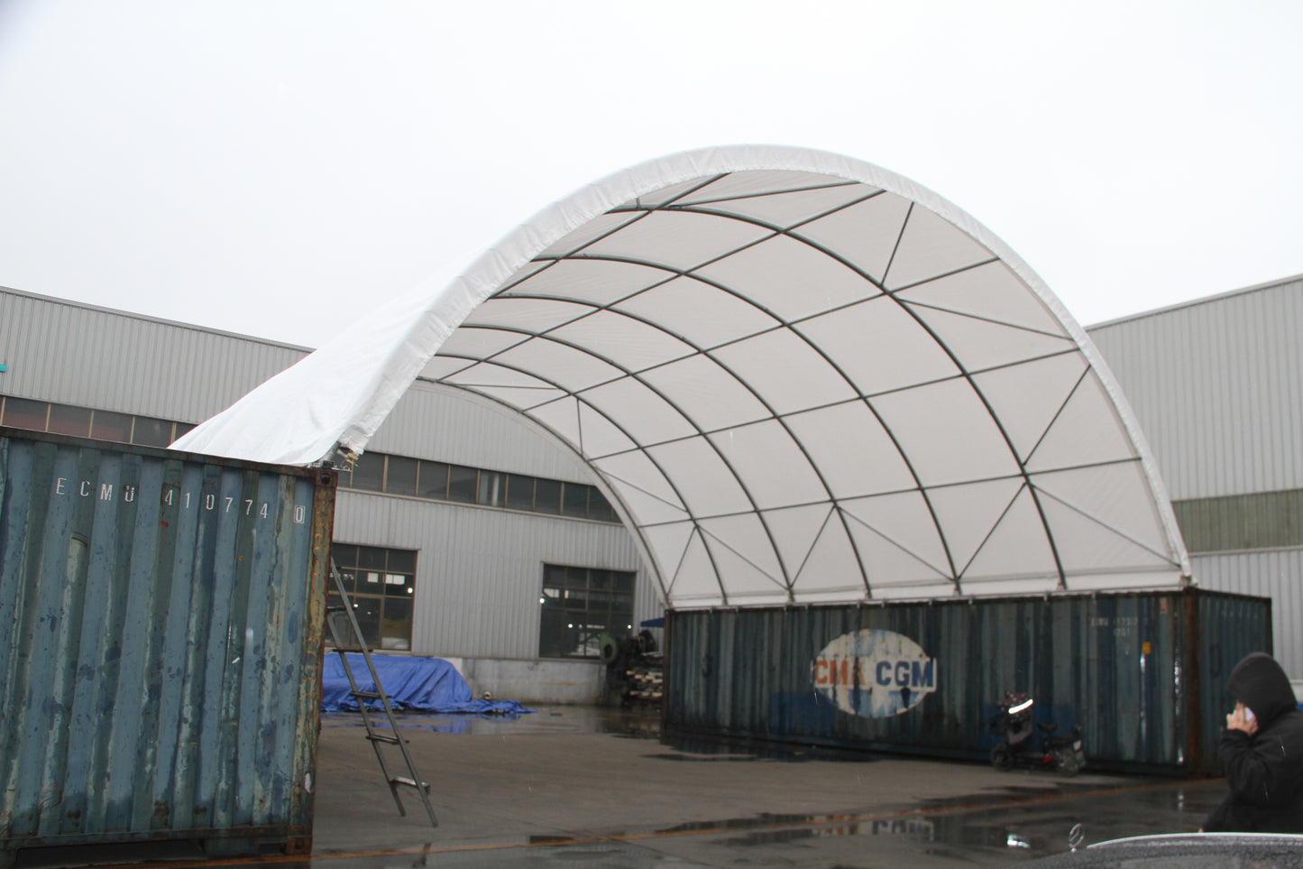 White fabric storage tent supported by metal frame set up over shipping containers