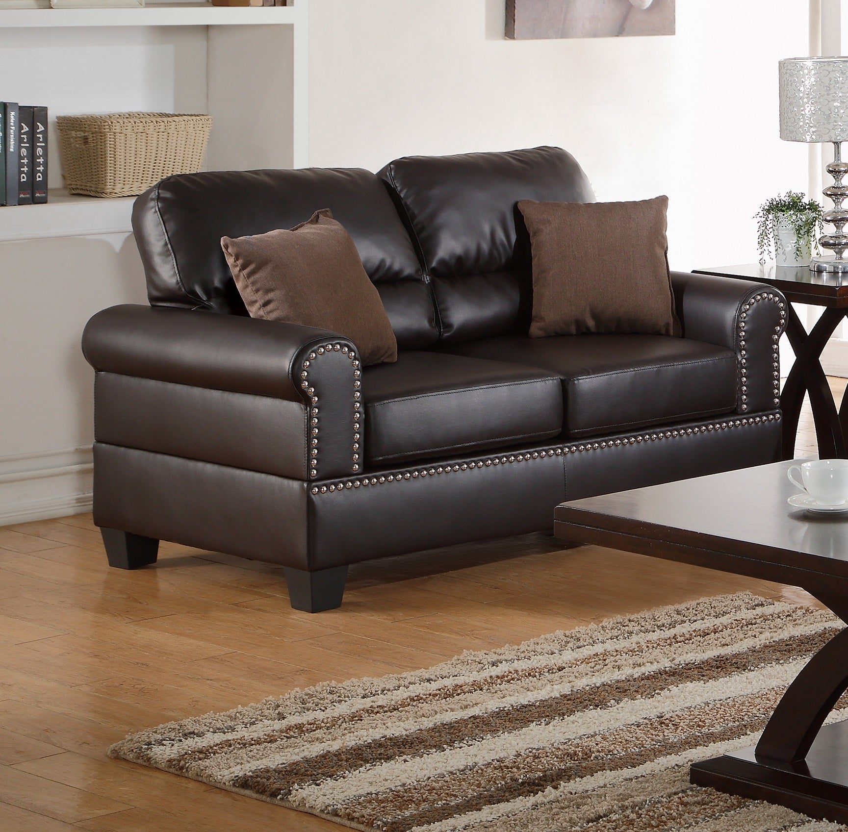 Dark brown faux leather loveseat with silver nailhead trim and matching throw pillows