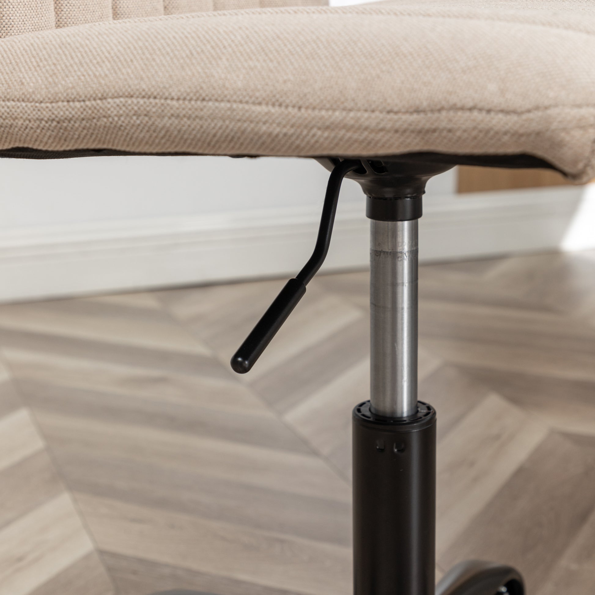 Closeup of a beige fabric office chair seat cushion with a height adjustment lever