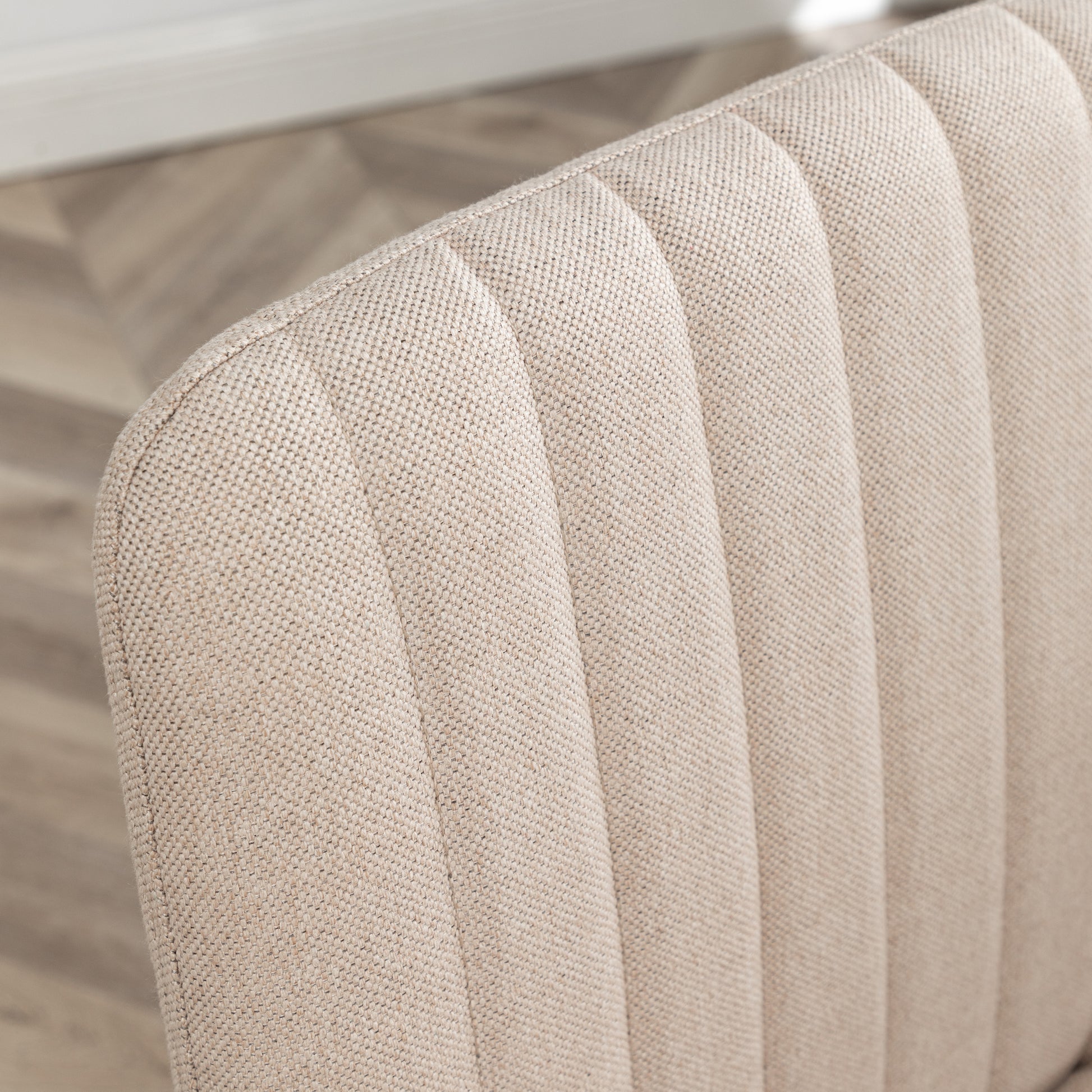Closeup of beige linen fabric with subtle channel tufting on a dining chair