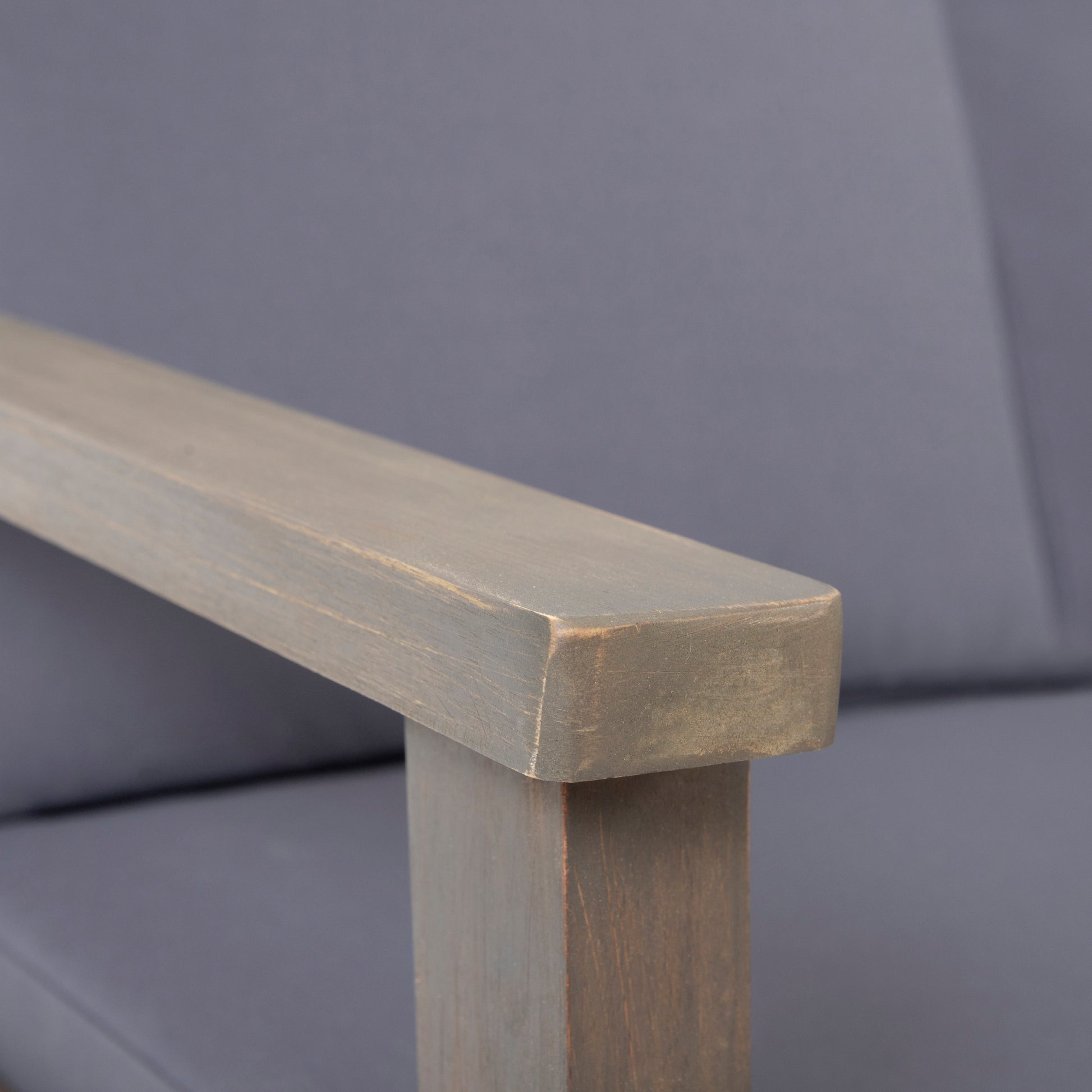 Closeup of a greywashed wood armchair armrest with textured fabric seating