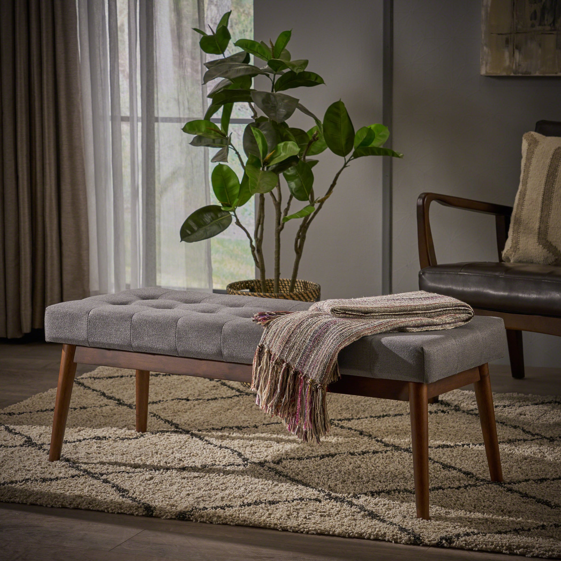 Tufted grey fabric ottoman with wooden legs and a woven throw for elegant entryway seating