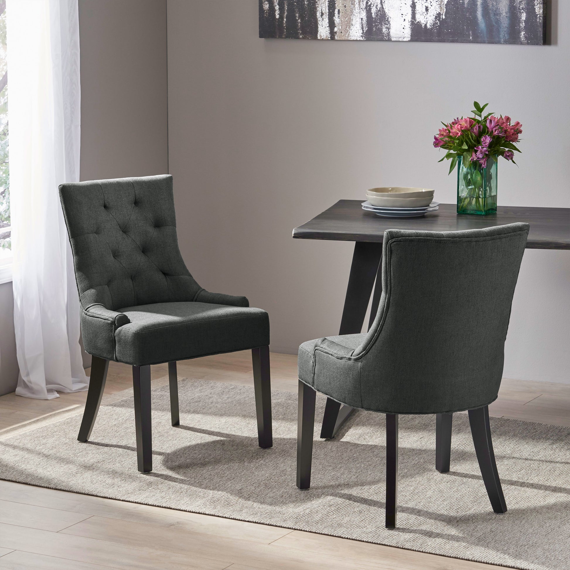 Two dark gray upholstered dining chairs with tufted backs and wooden legs