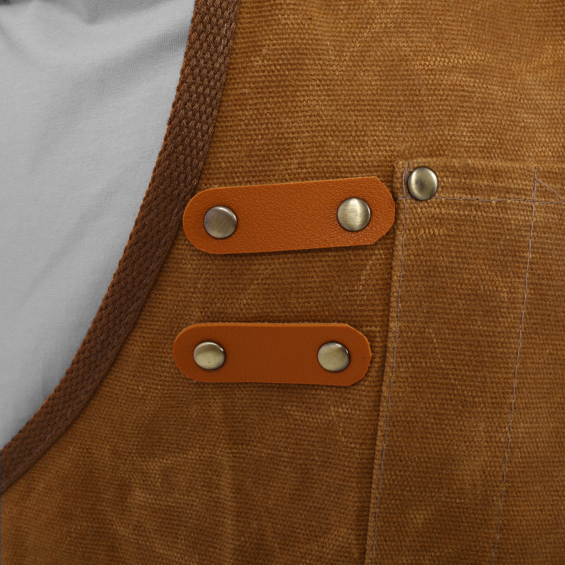 Brown canvas apron detail with tan leather straps and brass rivets