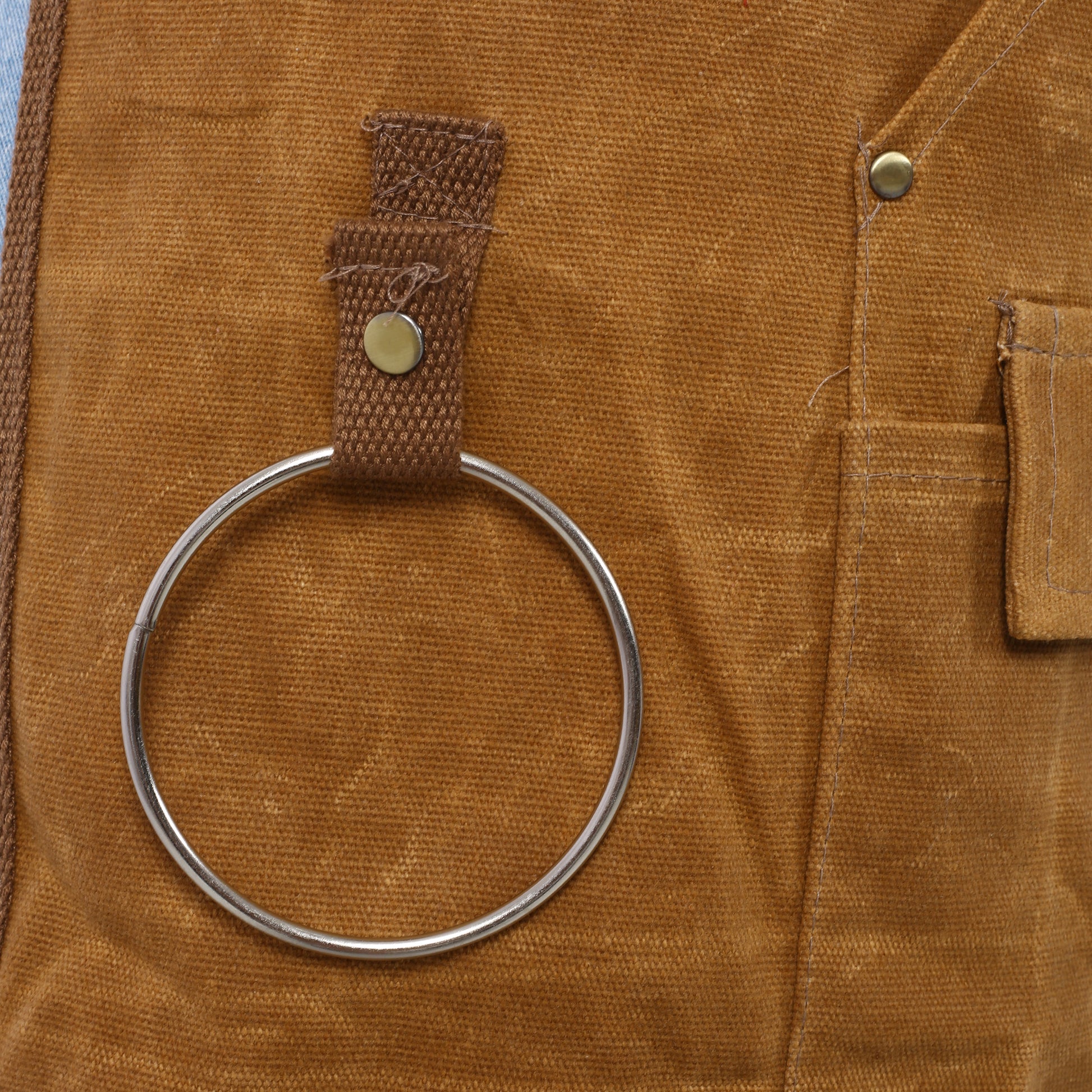 Brown canvas work apron detail with metal Dring for tool attachment