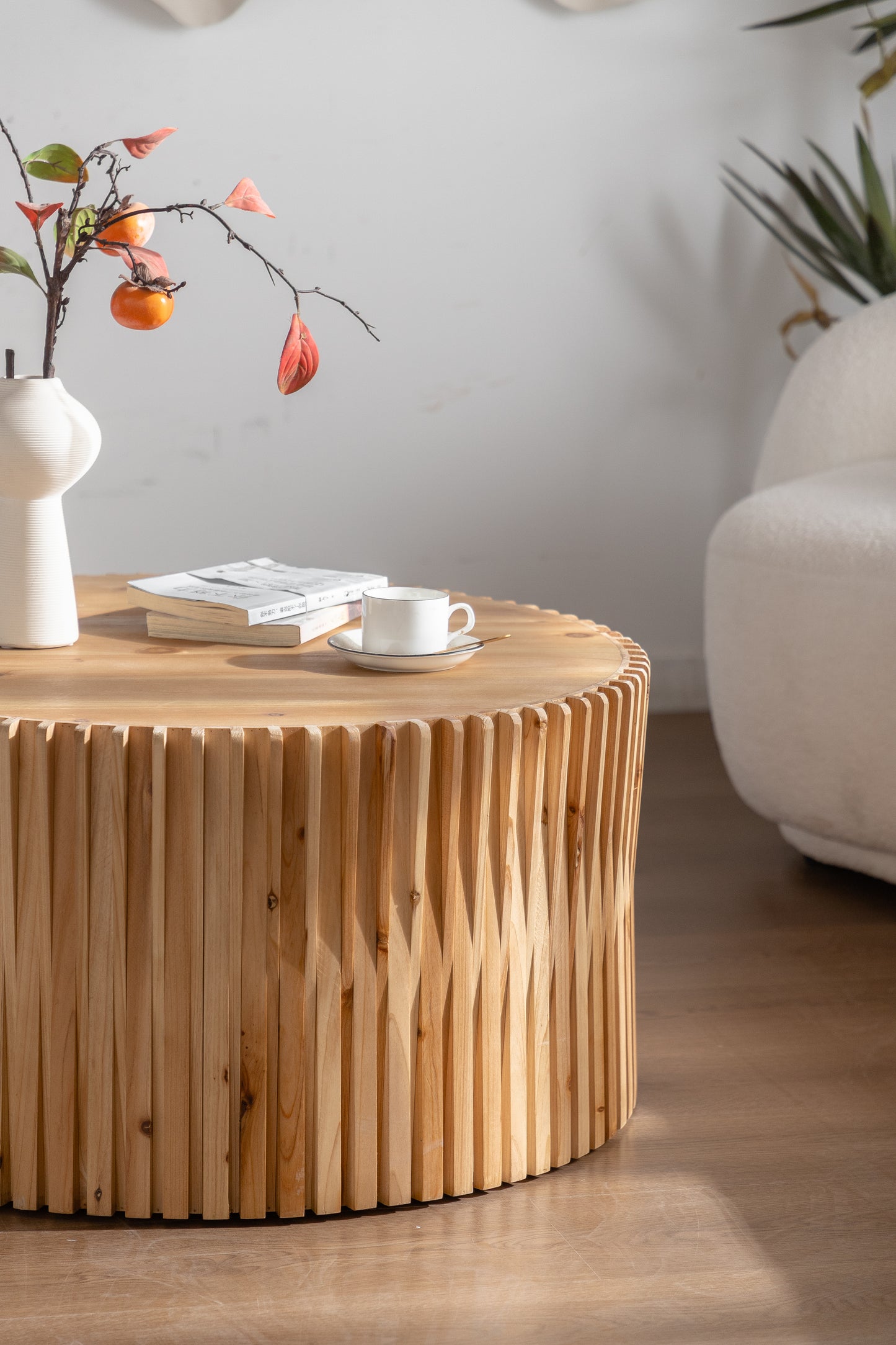 Round wooden coffee table with slatted base and books mug and decorative persimmon branch