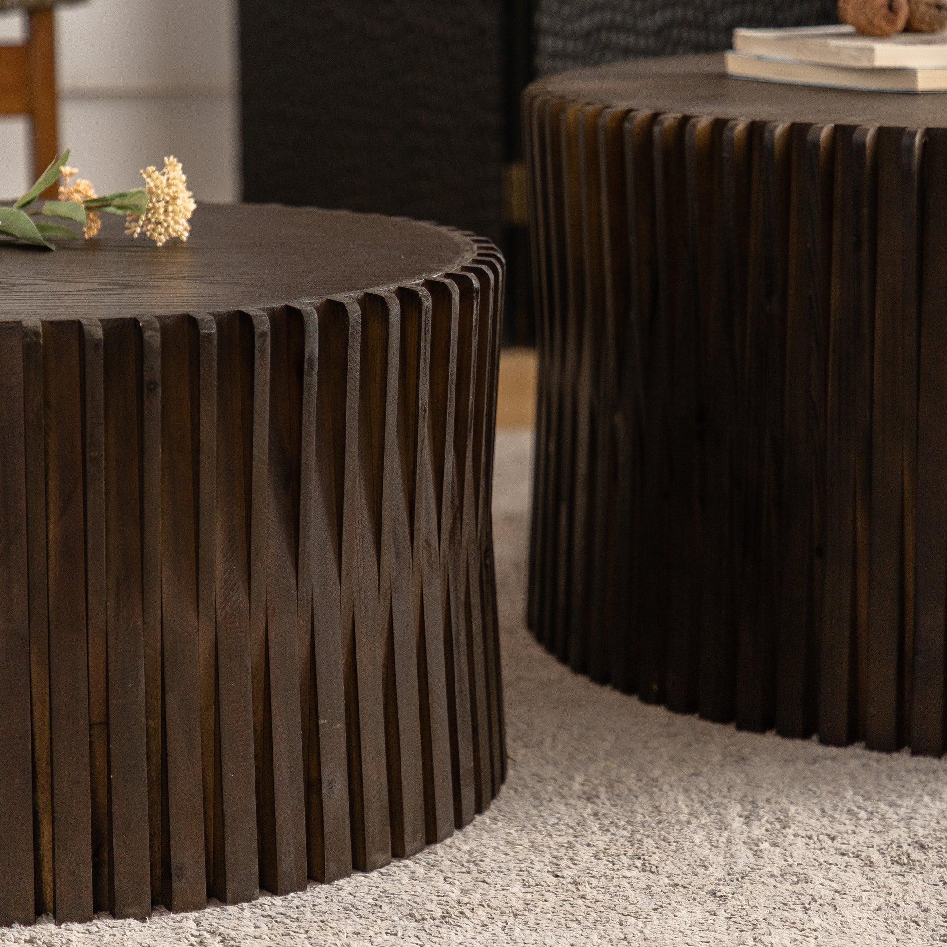 Round dark wood coffee table with vertical ribbed texture and a decorative sprig