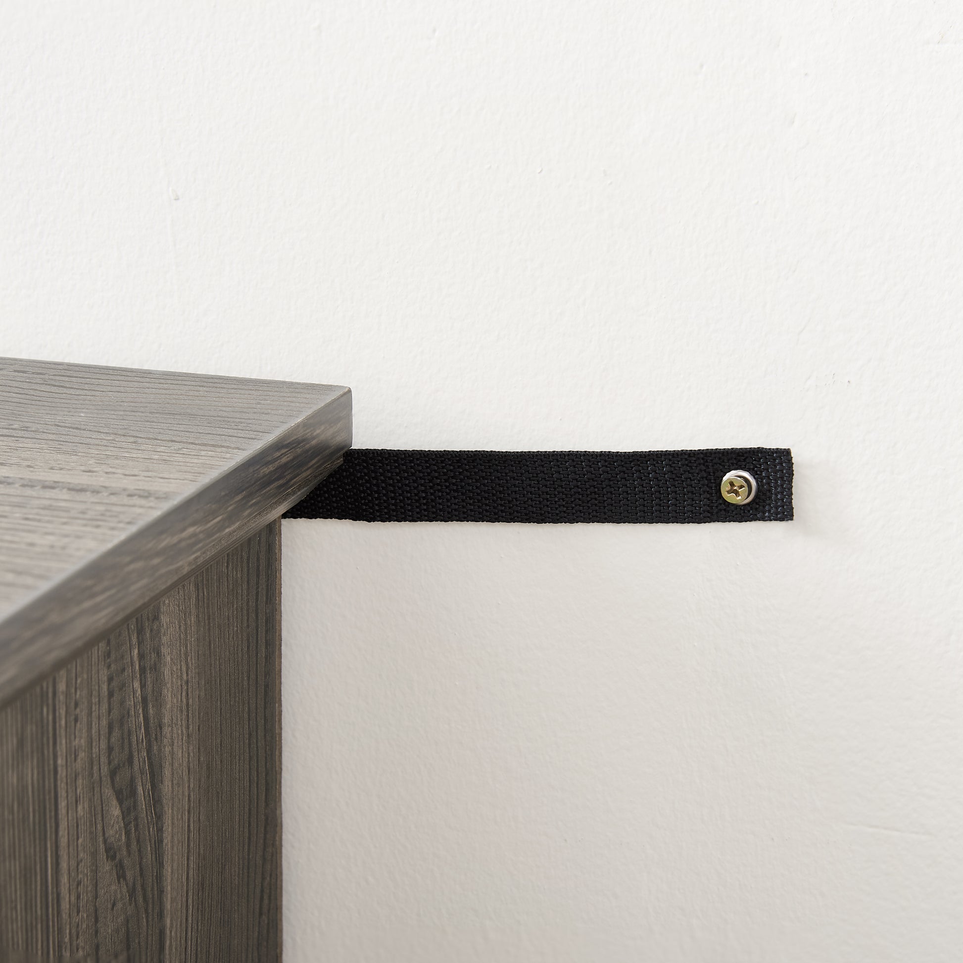 Gray wood shelf with a black antitip strap secured to the wall
