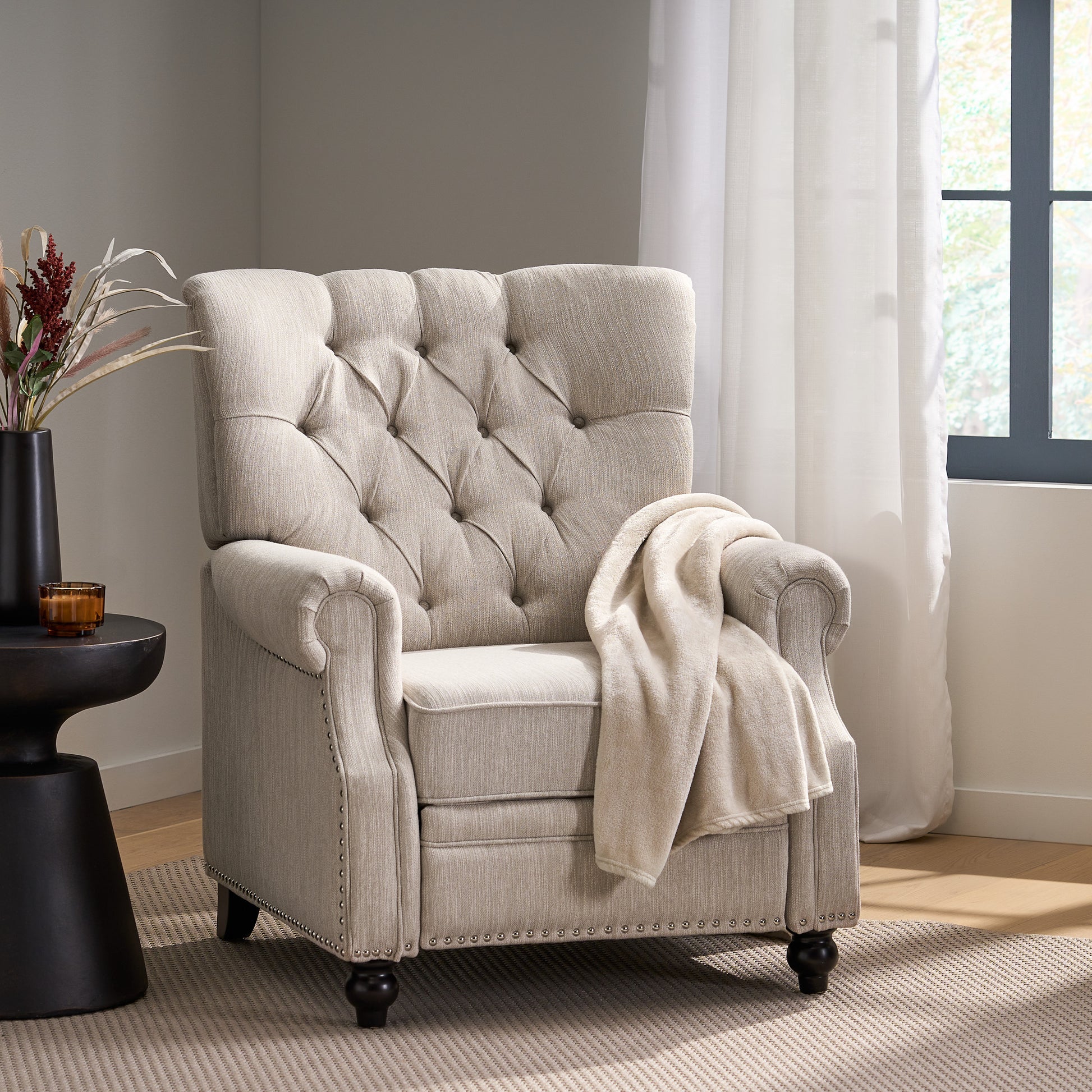 Beige upholstered recliner with tufted back and nailhead trim draped with a cream throw blanket