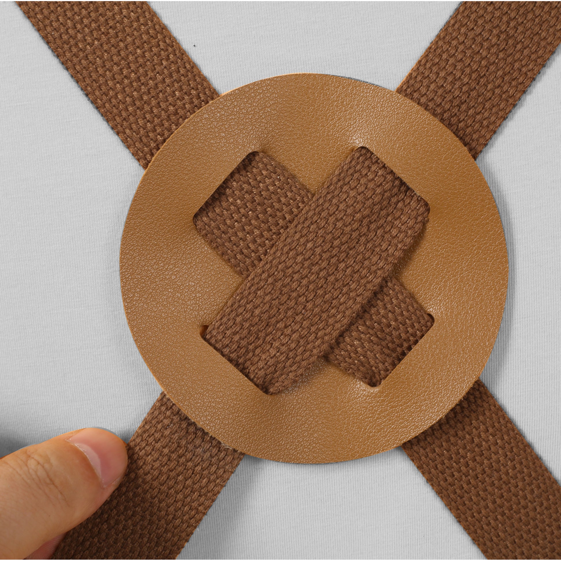 Brown canvas straps crossed over tan faux leather accent on a white shirt