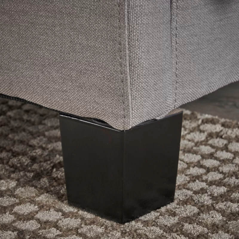 Closeup of a grey upholstered sofas square black wooden leg resting on a textured rug