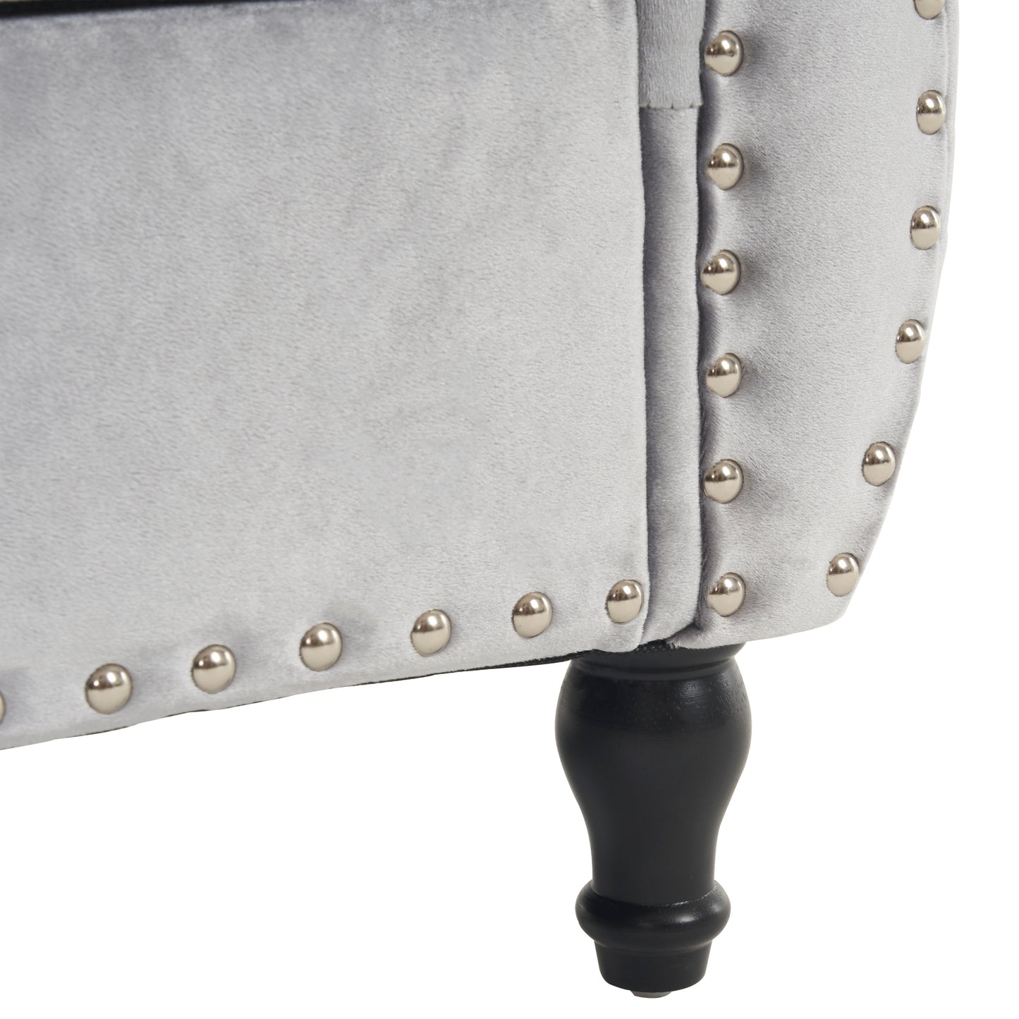 Closeup of a light gray velvet armchair with silver nailhead trim and a carved dark wood leg