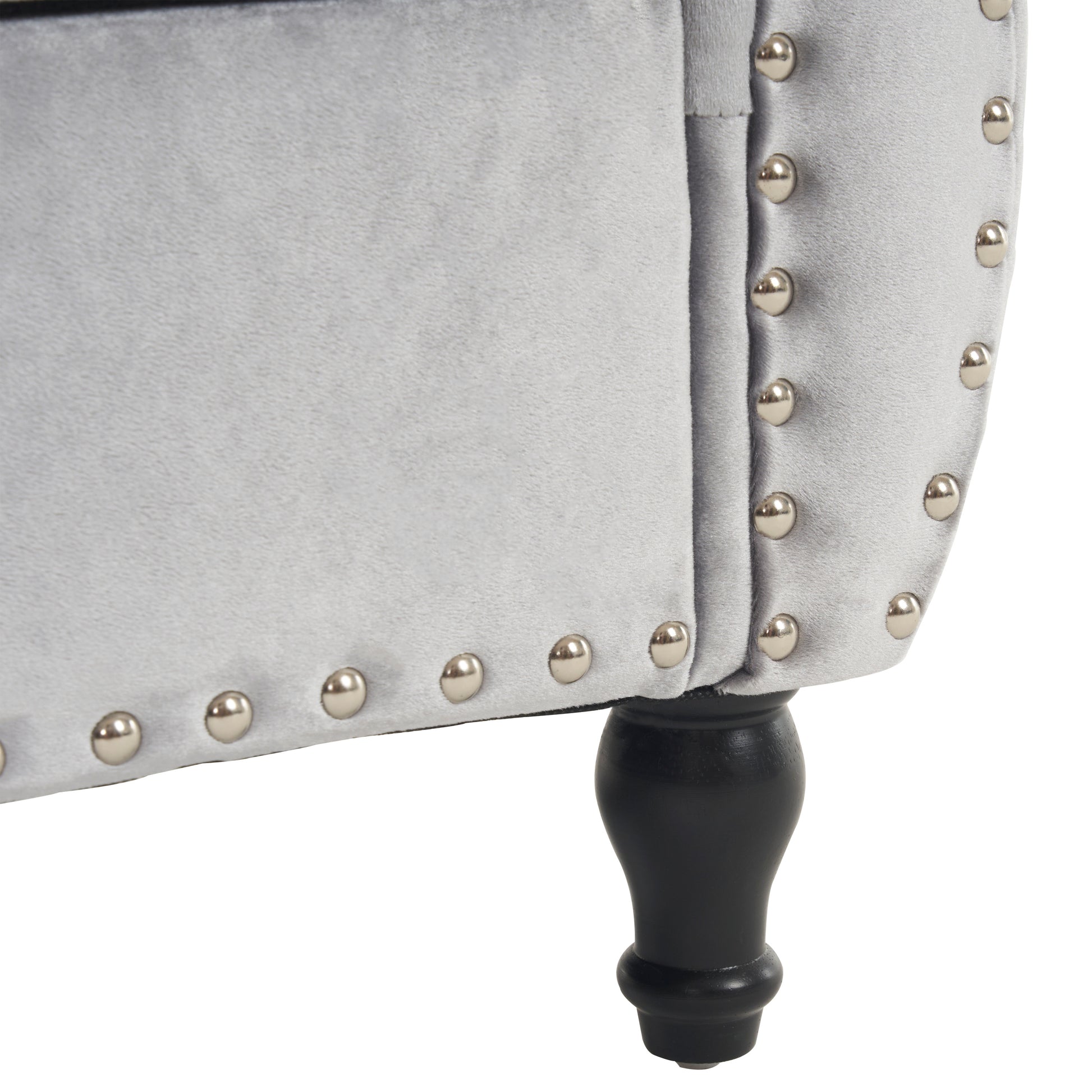 Closeup of a light gray velvet armchair with silver nailhead trim and a carved dark wood leg