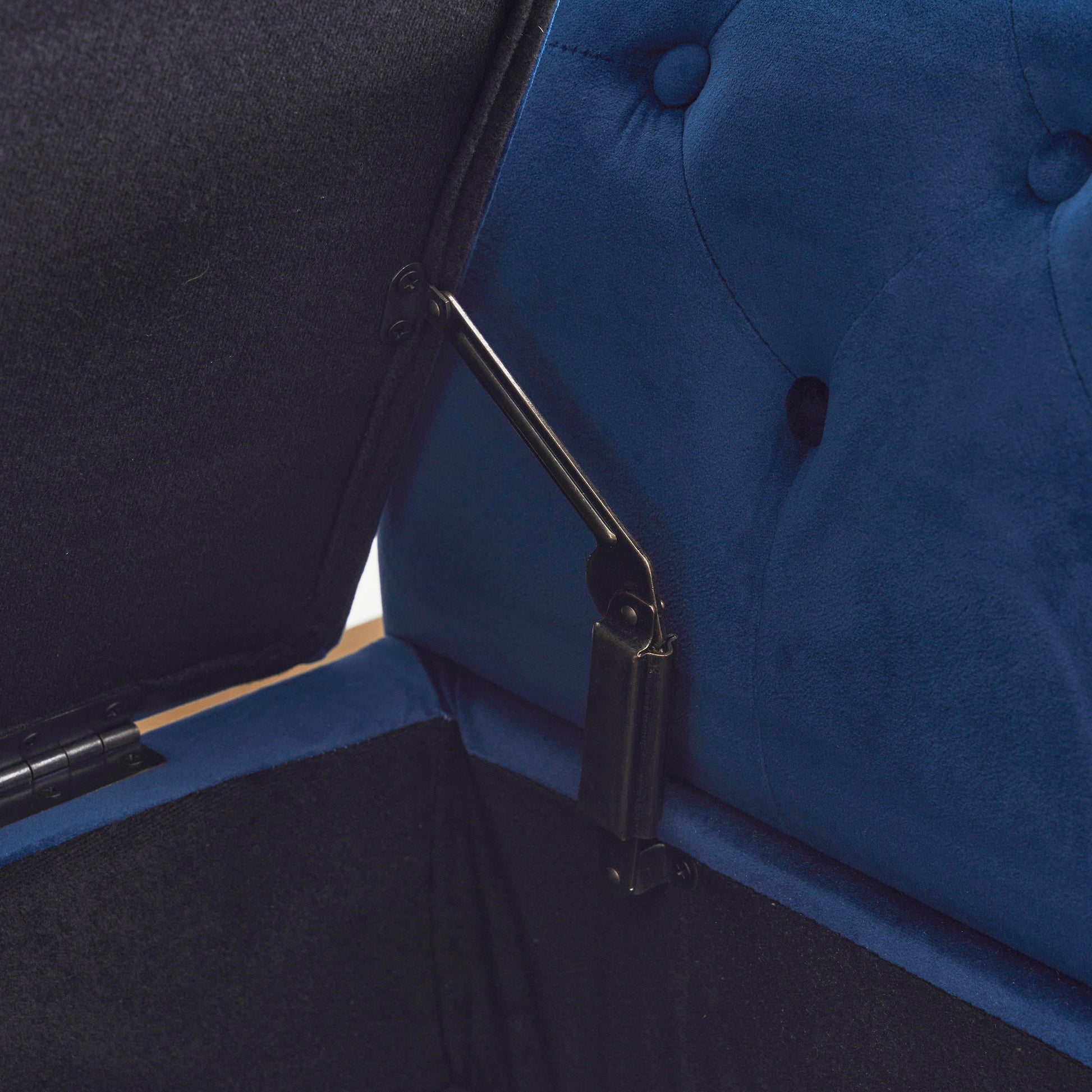 Closeup of a dark blue velvet storage ottoman with a metal hinge mechanism visible
