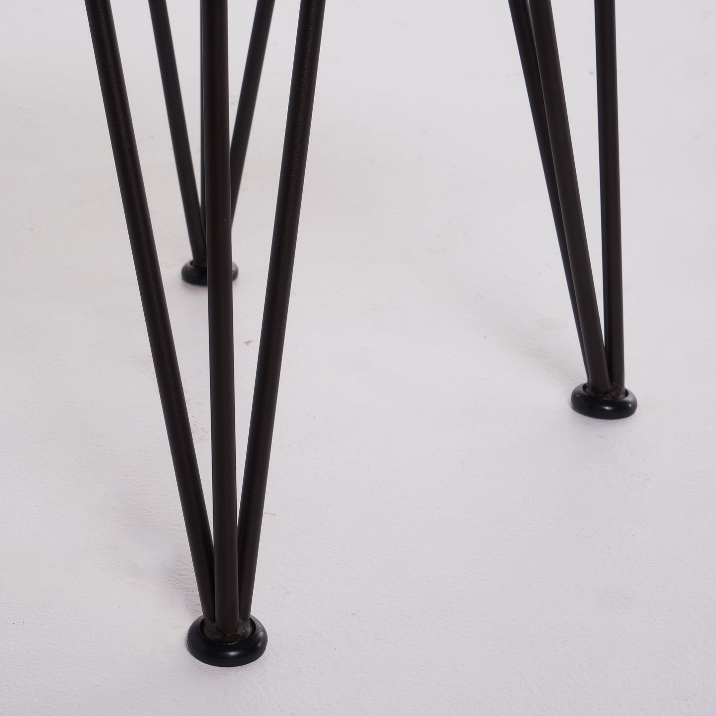Closeup of dark metal hairpin legs with black rubber feet on a white surface