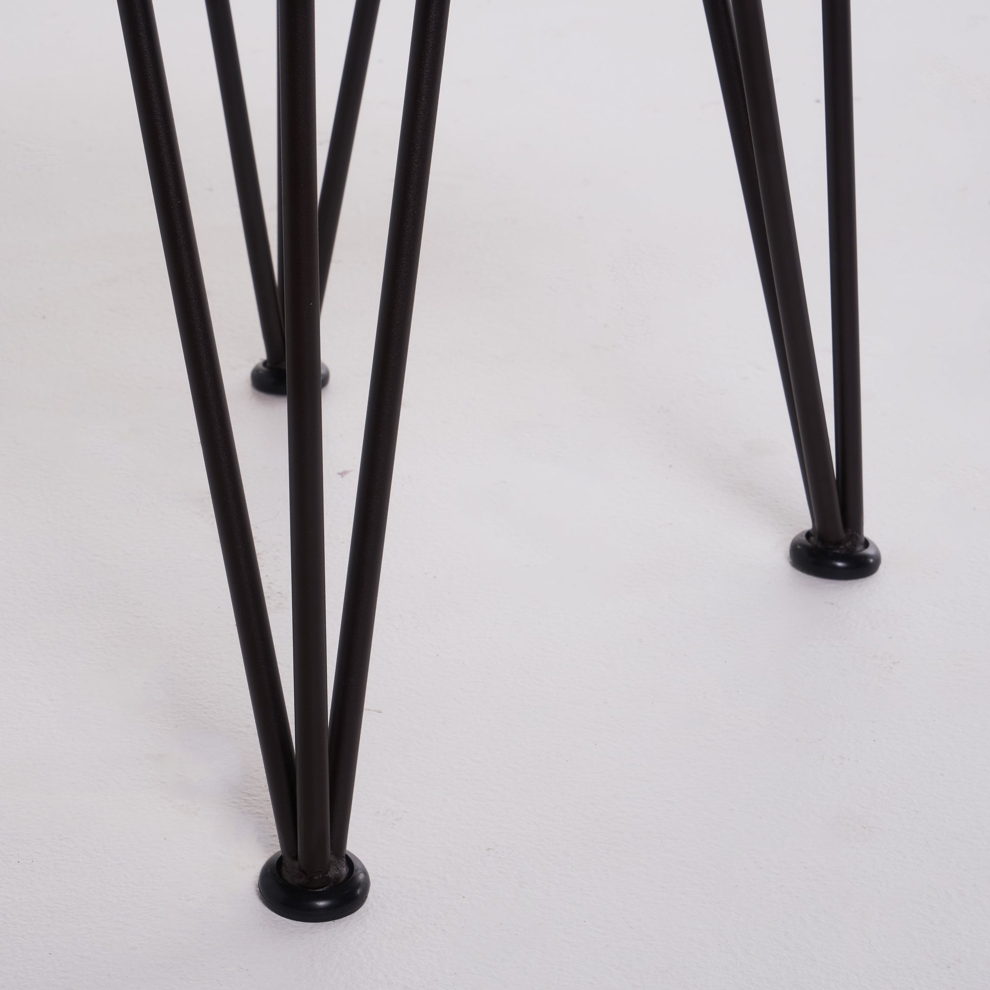 Closeup of dark metal hairpin legs with black rubber feet on a white surface