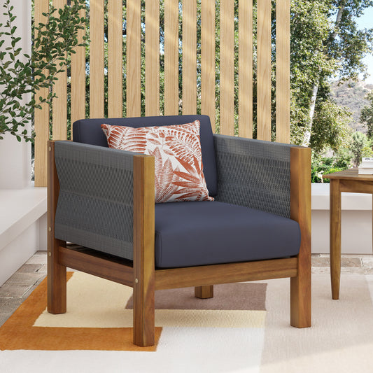 Dark gray woven outdoor armchair with navy blue cushions and a tropical leaf accent pillow