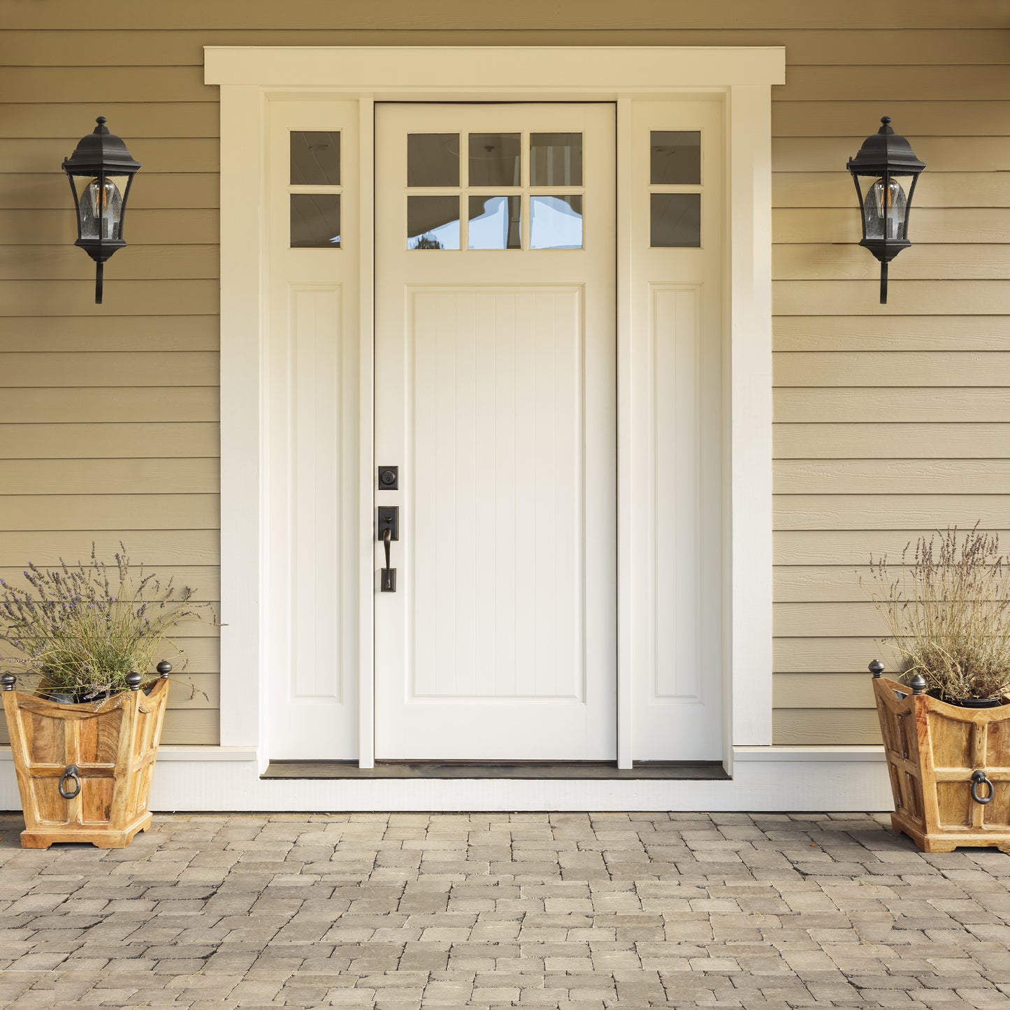 White wooden front door with sixpane glass transom flanked by black lanterns