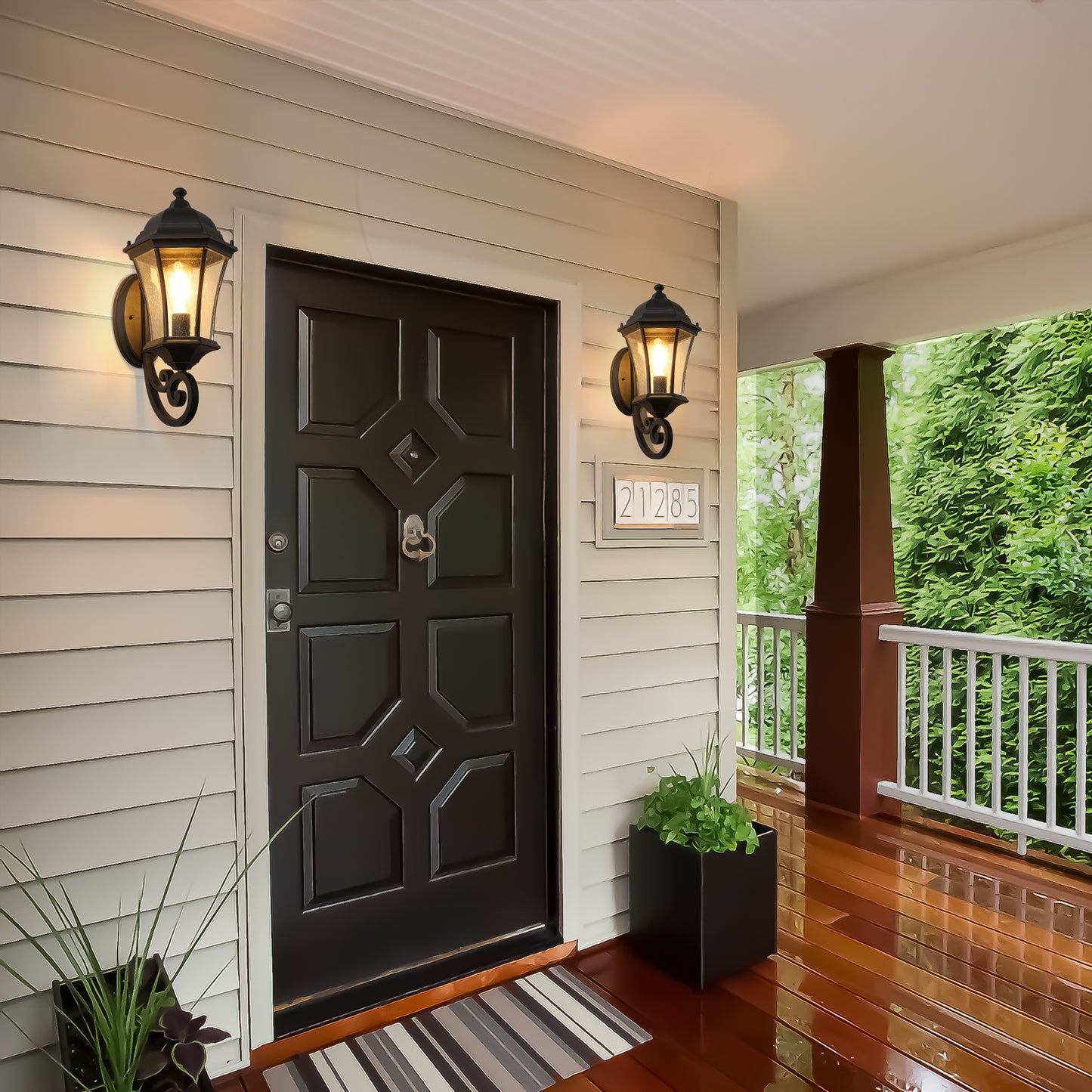 Black ornate lantern sconce with clear glass panels casting a warm glow on a beige exterior wall