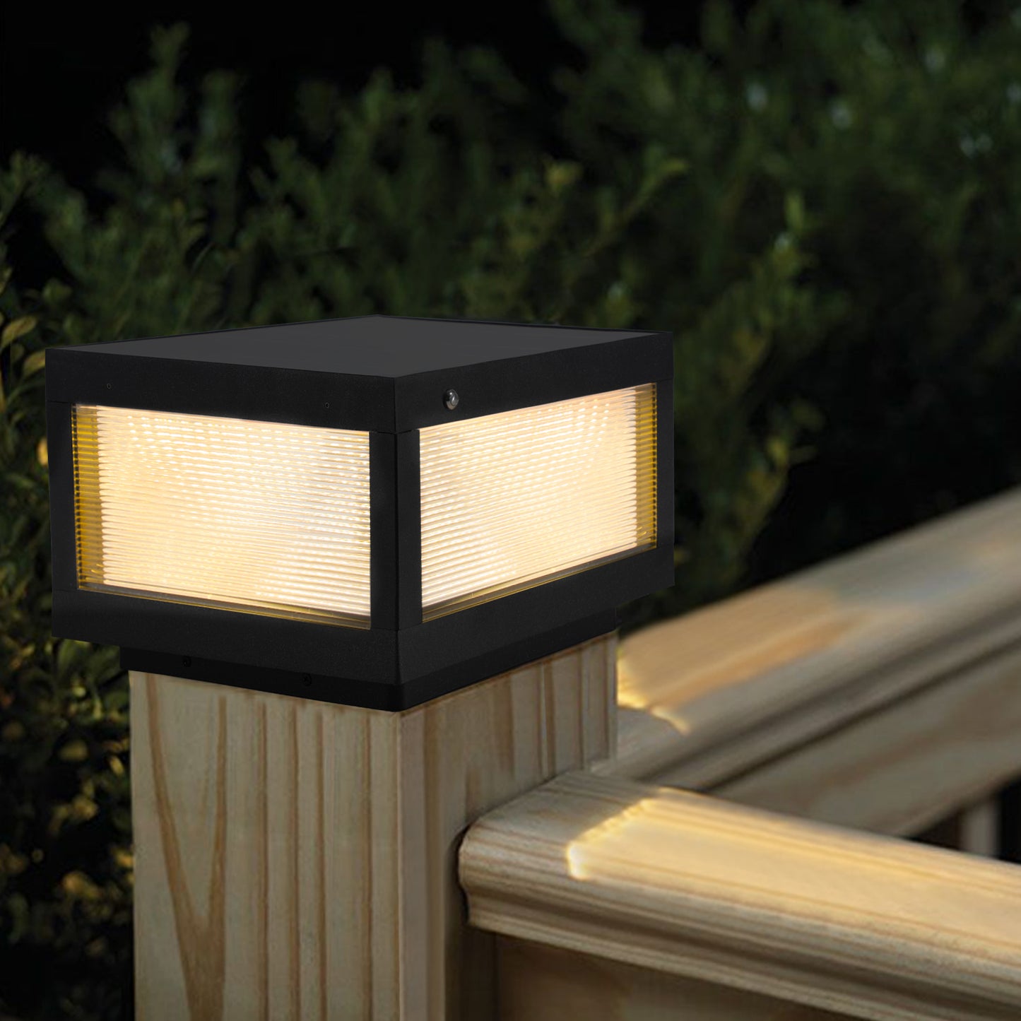Modern black aluminum deck light with clear ribbed glass casting warm yellow light downwards