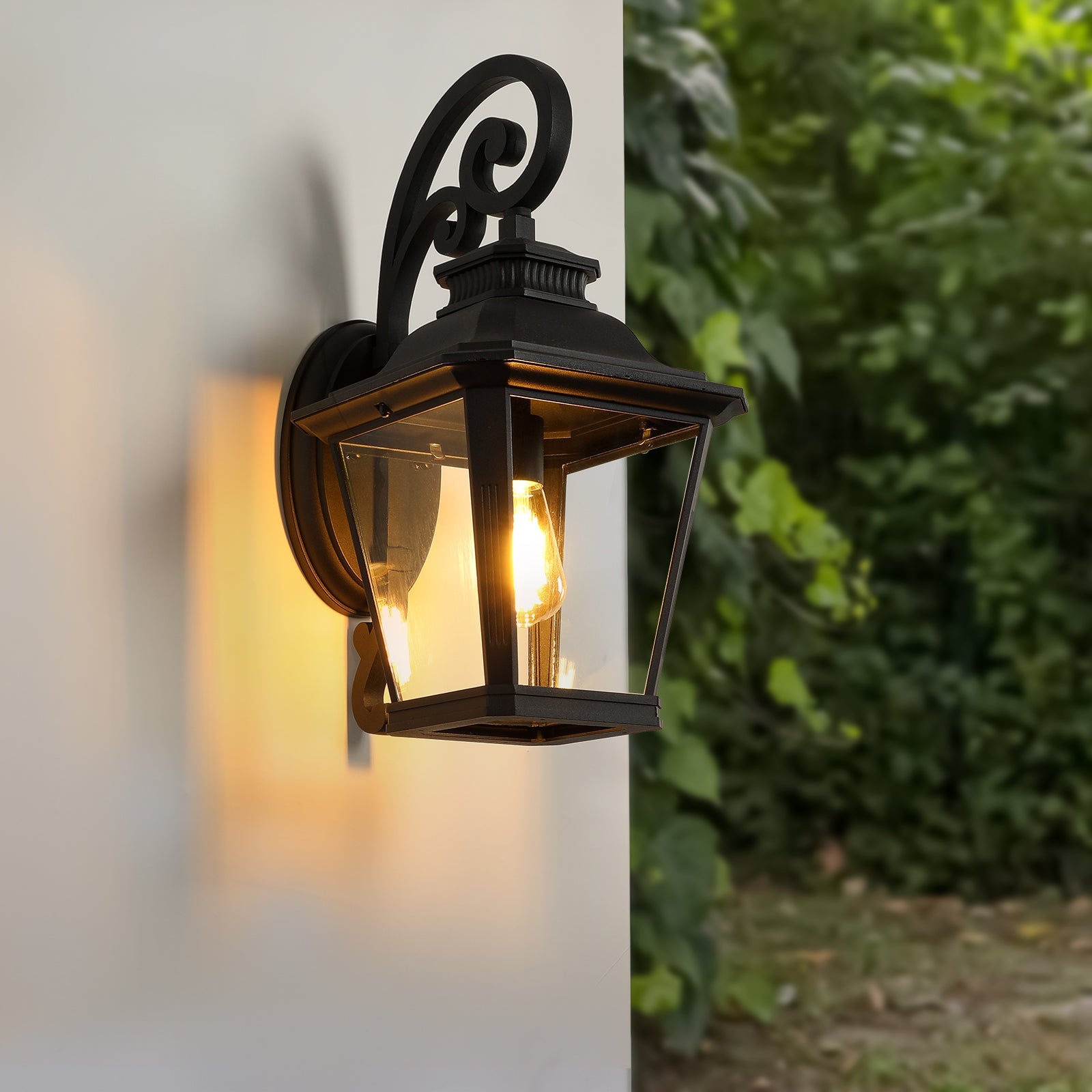 Black metal outdoor lantern with clear glass panels and a decorative scrolled arm