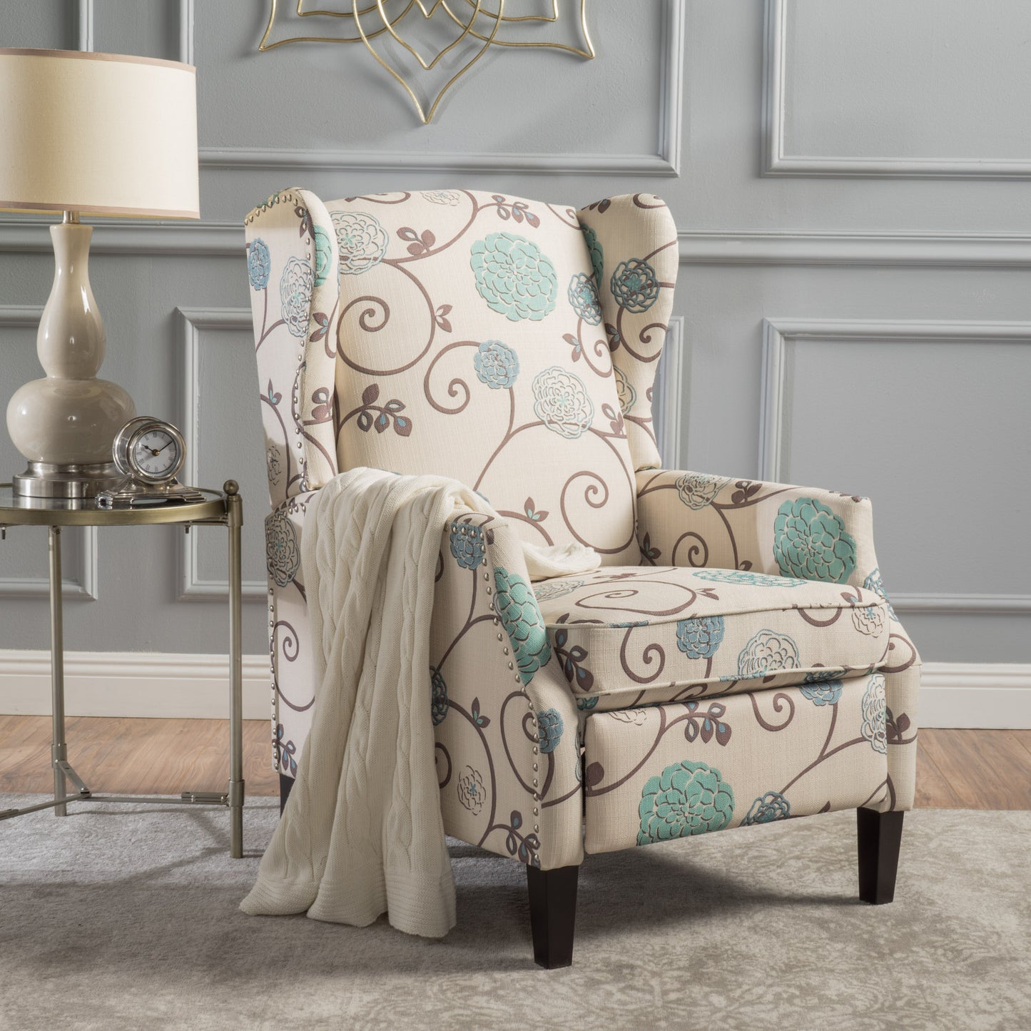 Cream wingback chair with floral pattern and studded trim featuring a beige throw blanket