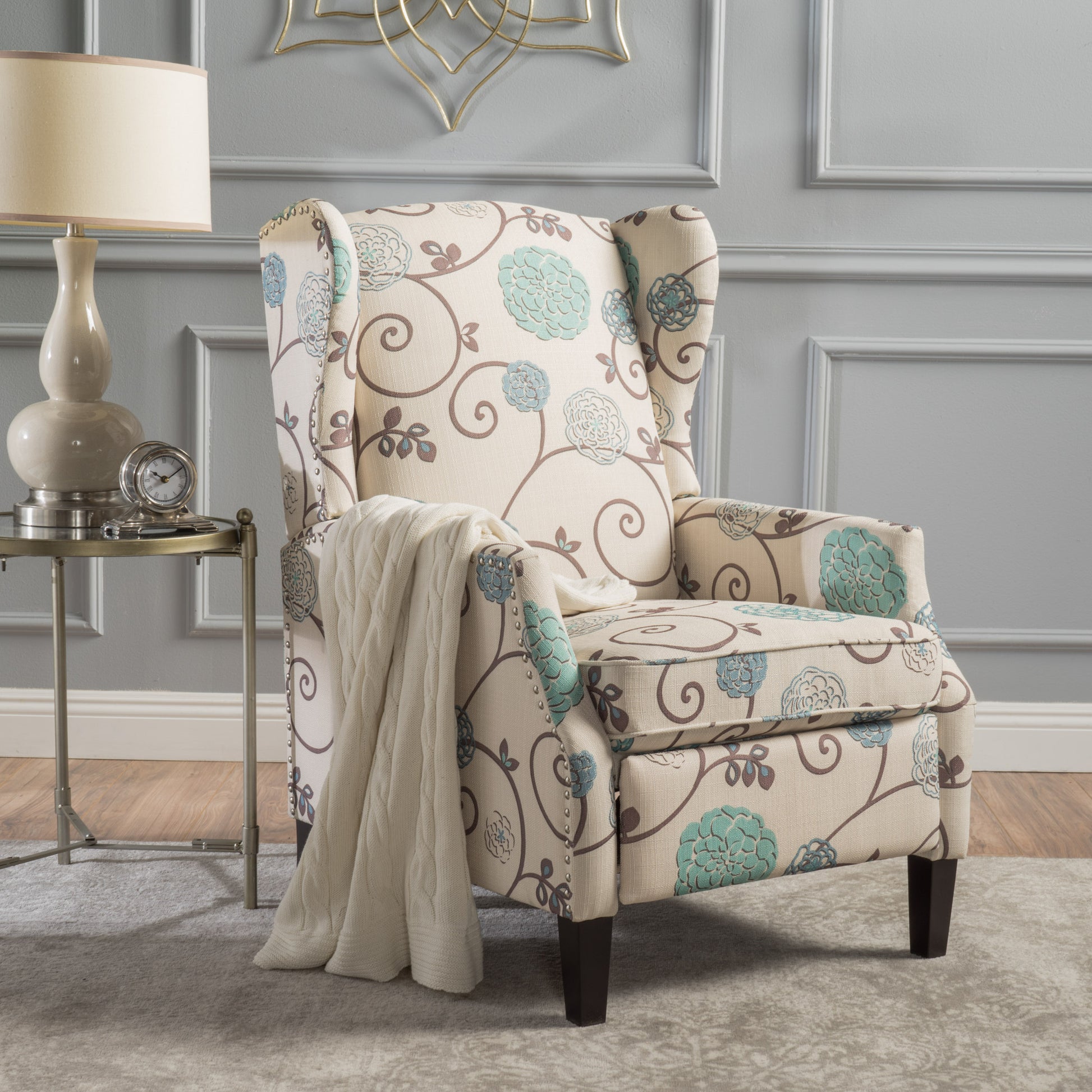 Cream wingback chair with floral pattern and studded trim featuring a beige throw blanket