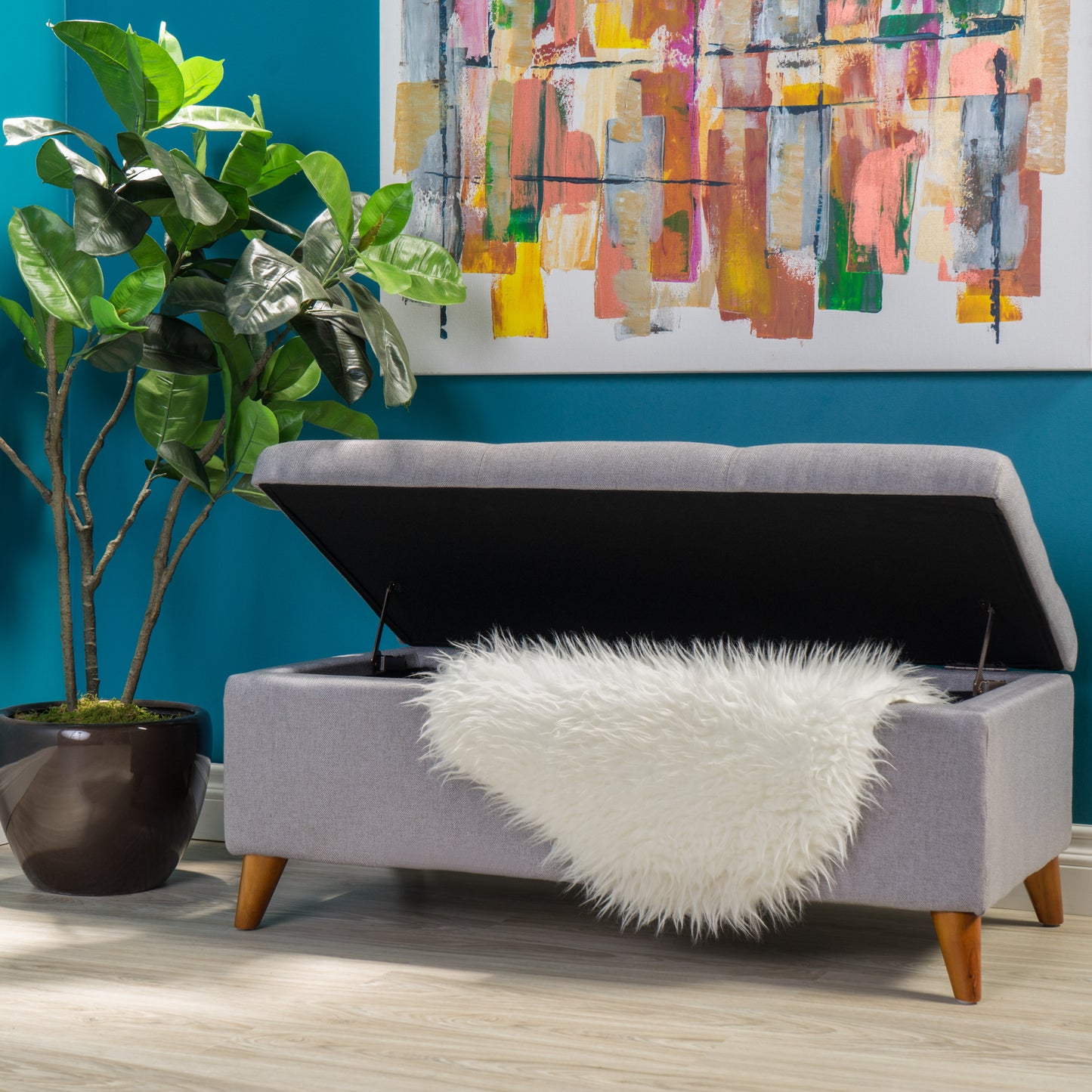 Gray fabric storage ottoman with hinged lid and plush white accent throw