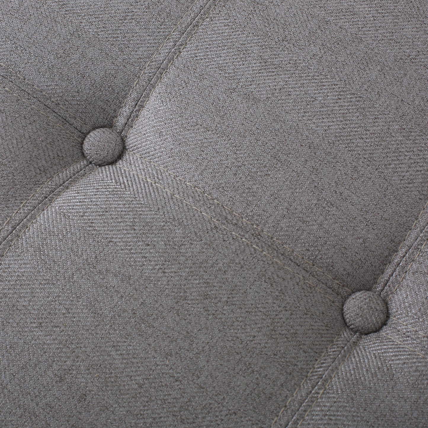 Closeup of grey woven fabric with tufted buttons and contrasting stitching