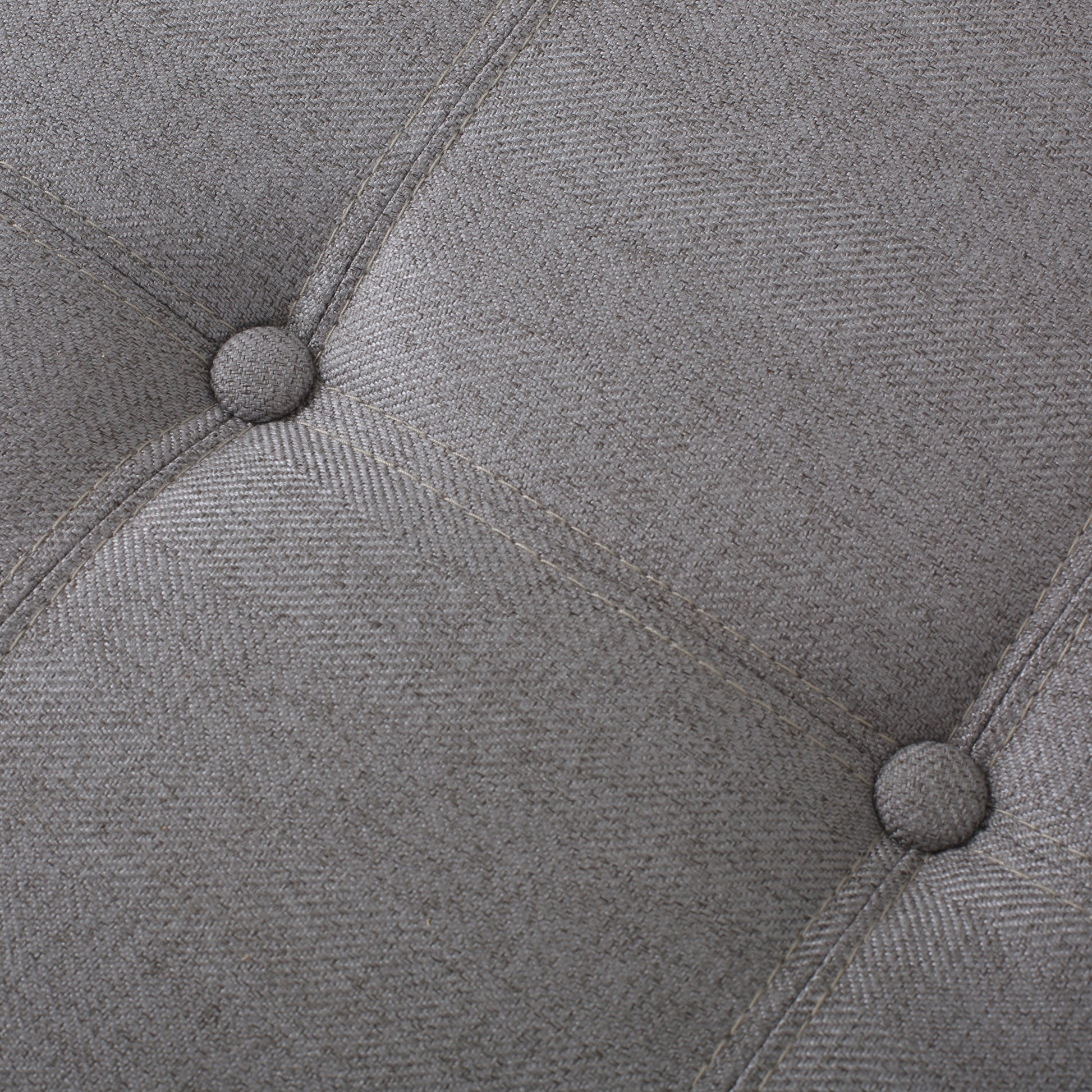 Closeup of grey woven fabric with tufted buttons and contrasting stitching