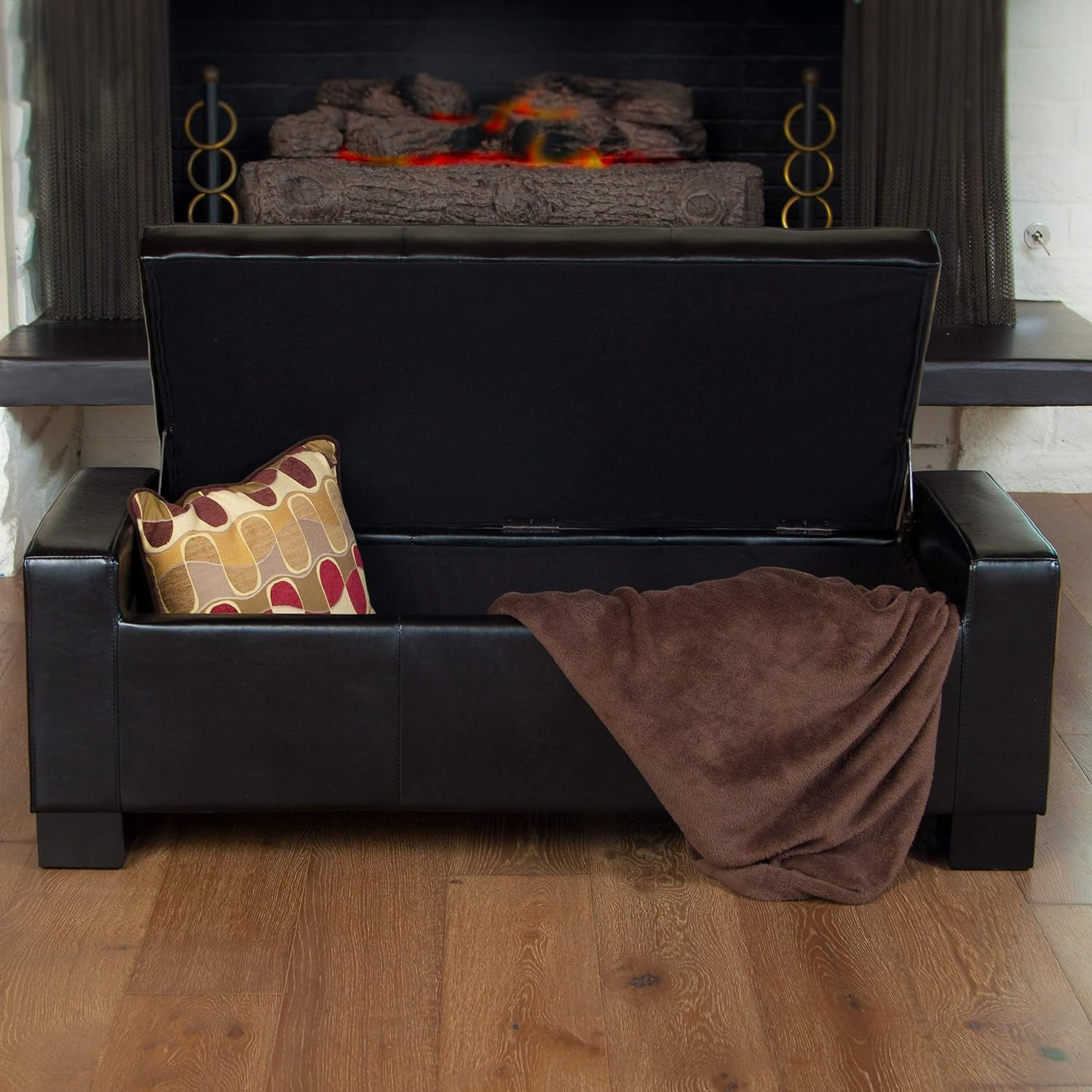 Black faux leather storage ottoman with open lid pillow and blanket