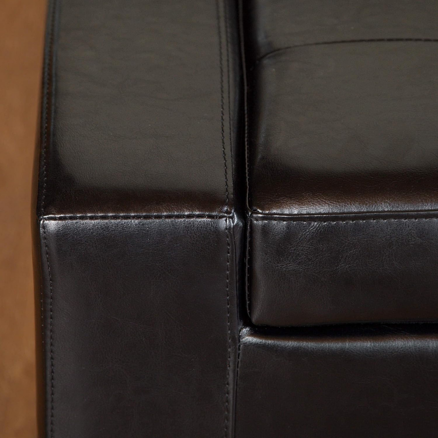 Closeup of a dark brown leather upholstered ottoman corner with stitching details