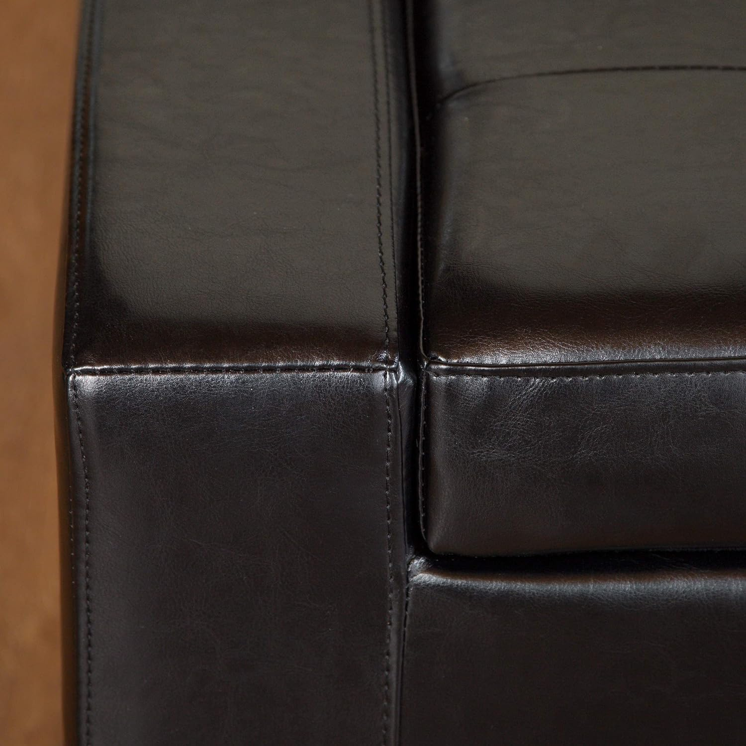 Closeup of a dark brown leather upholstered ottoman corner with stitching details