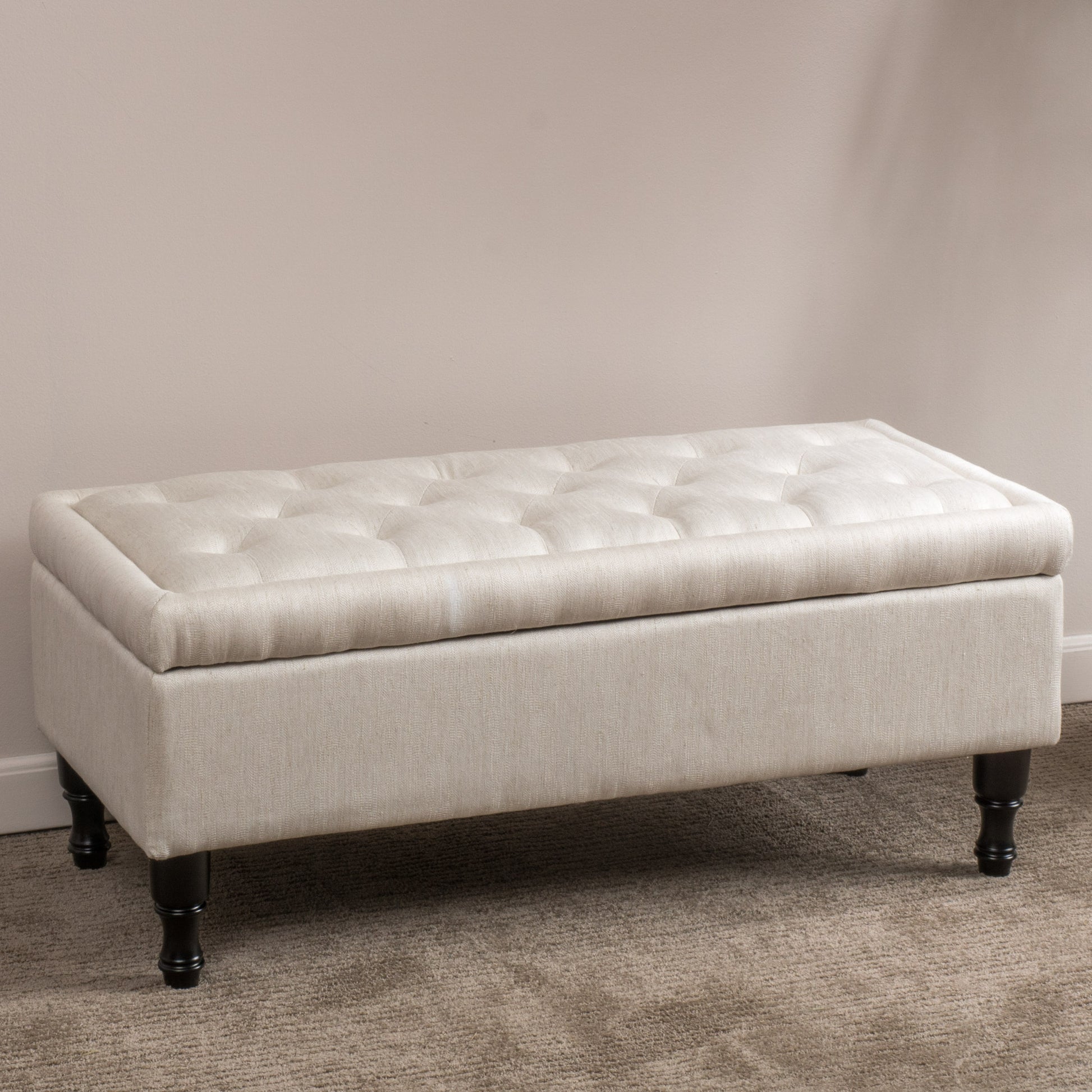 Tufted linen storage ottoman in a neutral beige color featuring dark wooden legs and a classic design