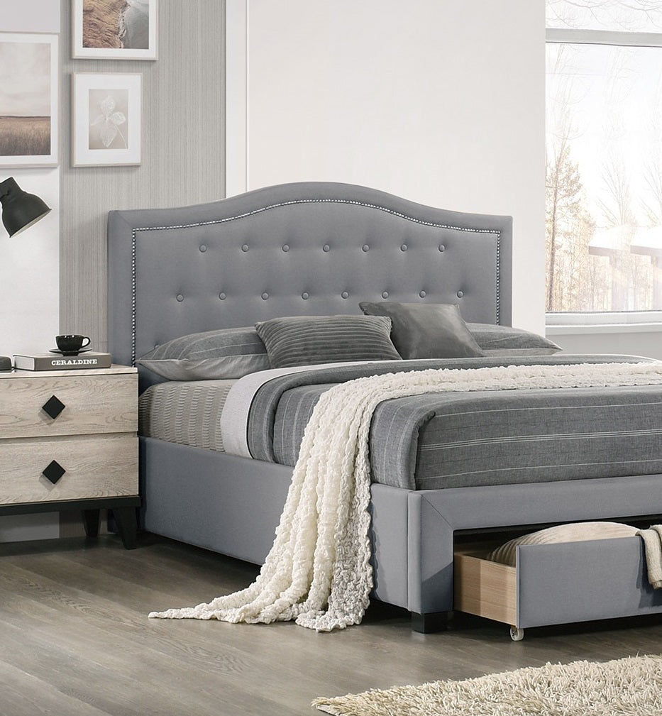 Grey upholstered bed with diamond tufting and silver nailhead trim A plush cream throw rests on the grey bedding accentuating this queen bed