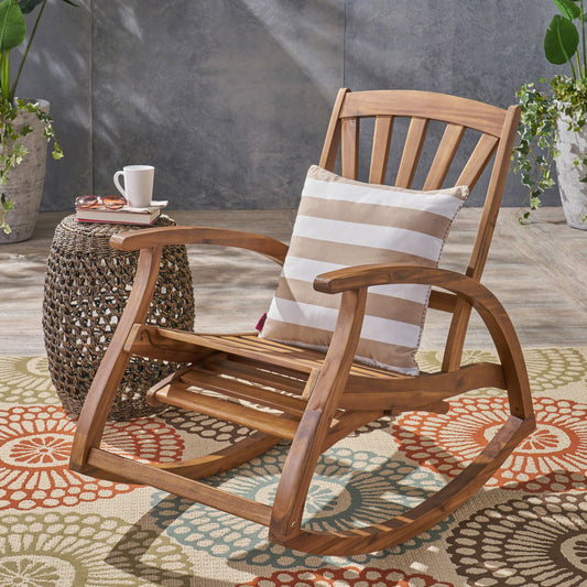 A sturdy wooden rocking chair with a striped cushion sits on an outdoor rug