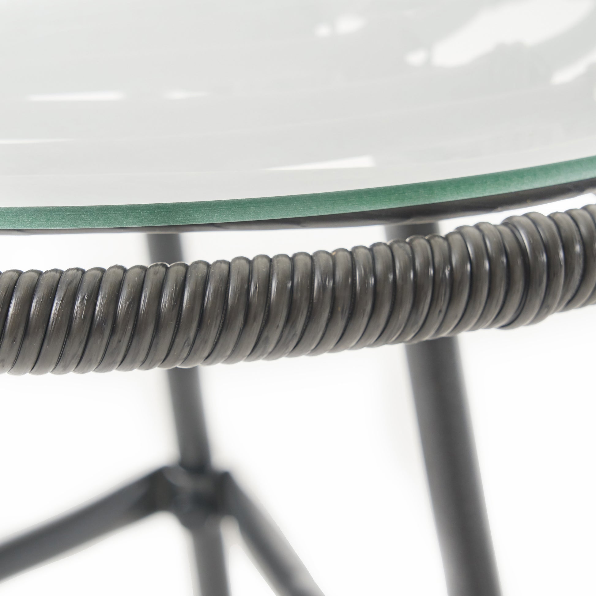 Closeup of a dark gray wicker weave on a chair armrest and clear glass tabletop