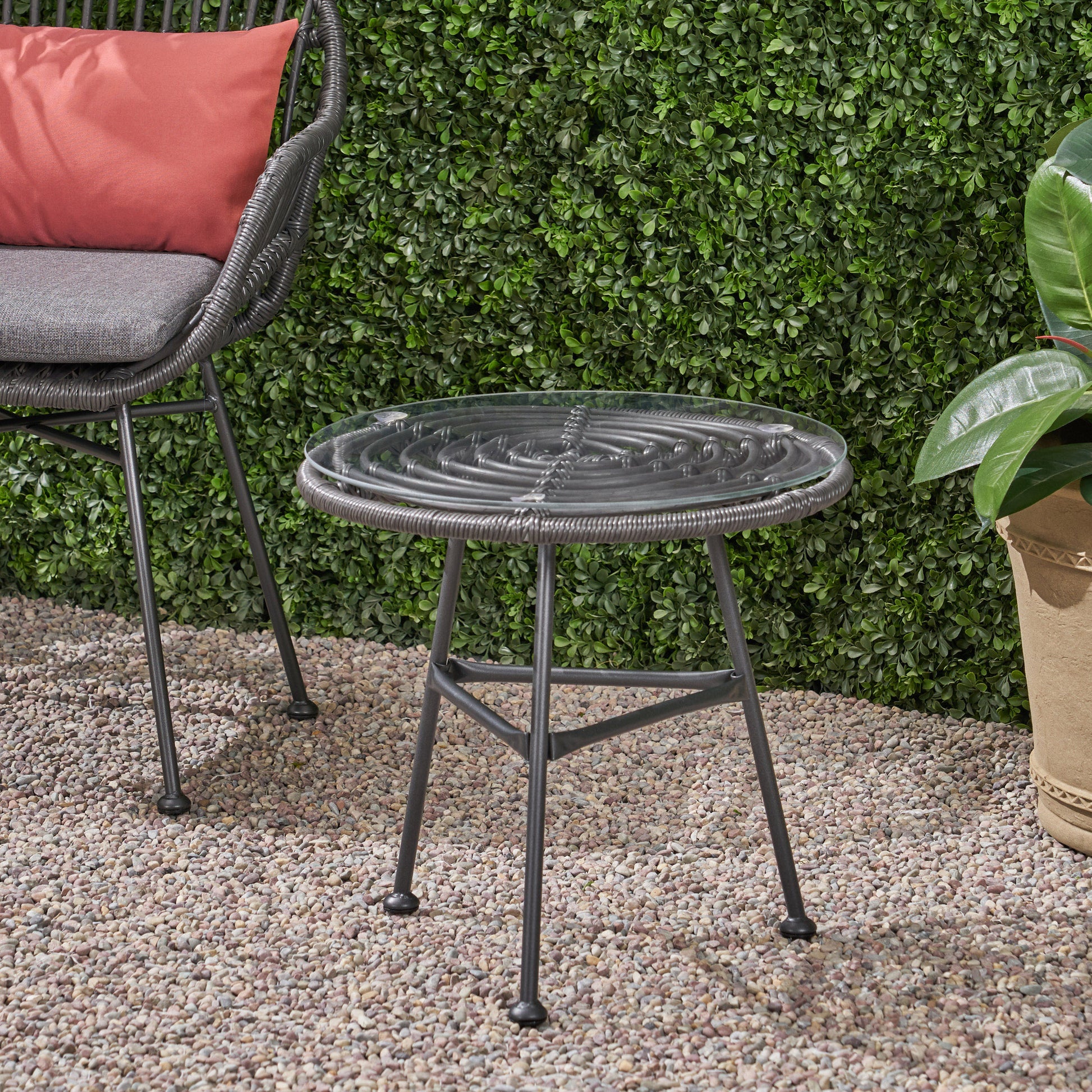 Round wicker side table with a clear glass top and dark metal legs perfect for outdoor patios
