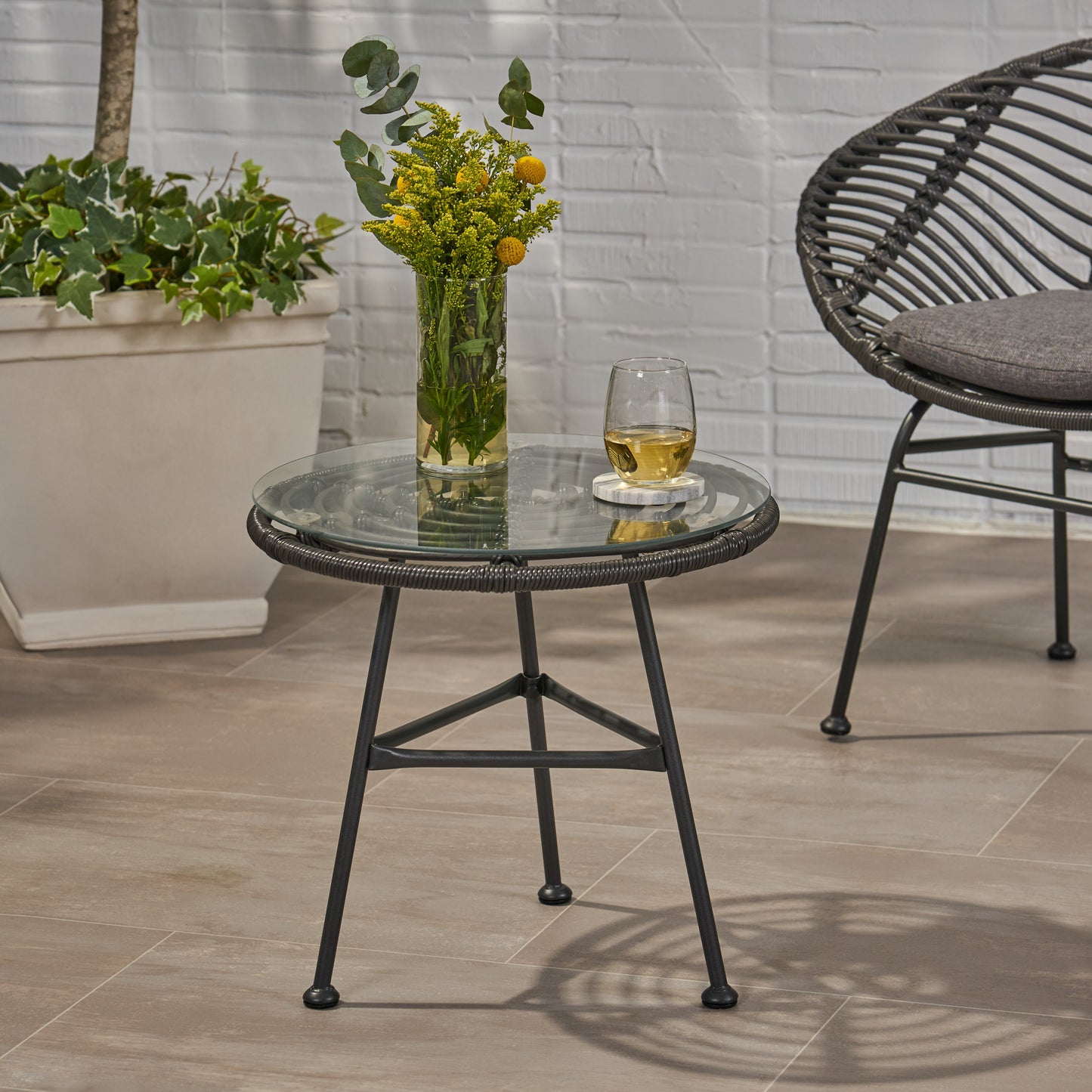 Round glass top patio accent table with dark gray wicker and metal legs