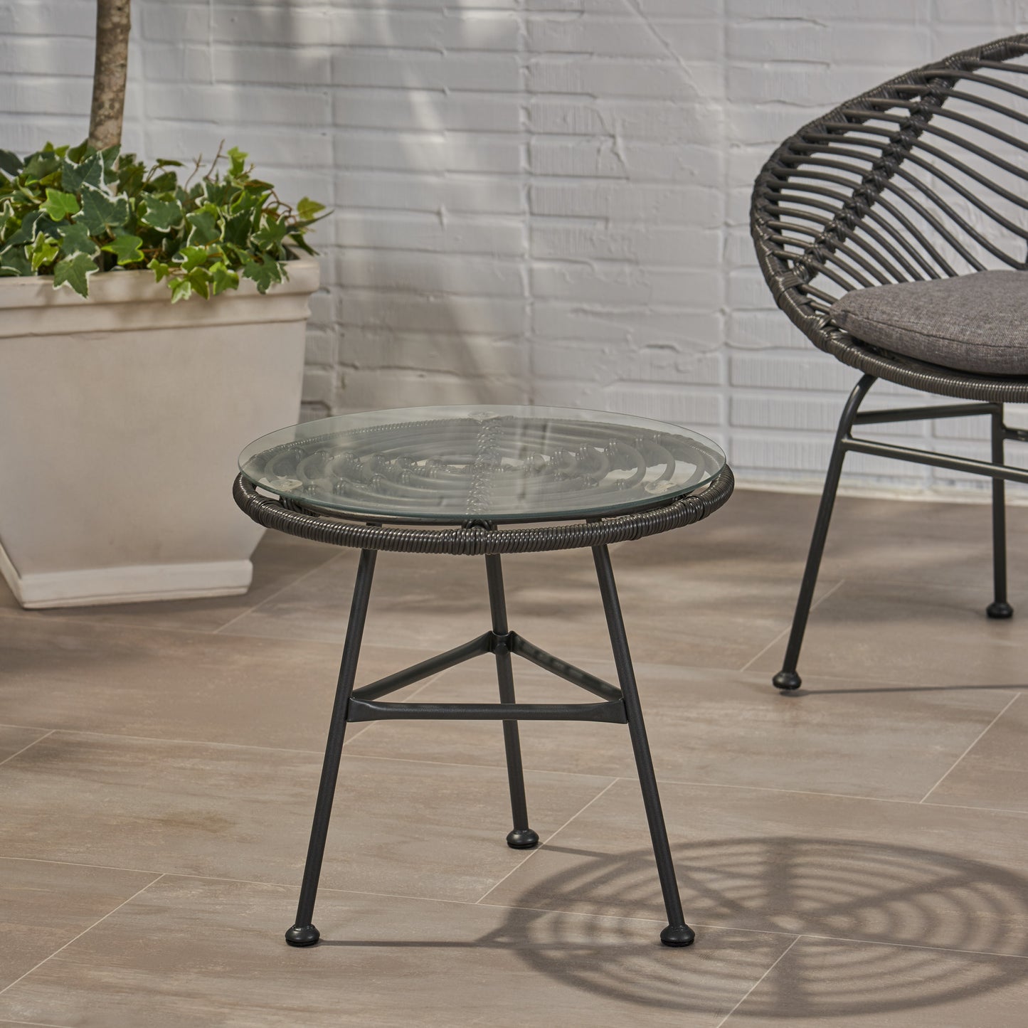 Round woven outdoor side table with glass top and dark metal legs