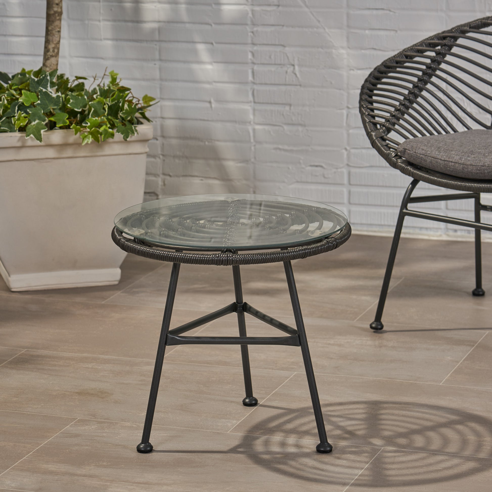 Round woven outdoor side table with glass top and dark metal legs