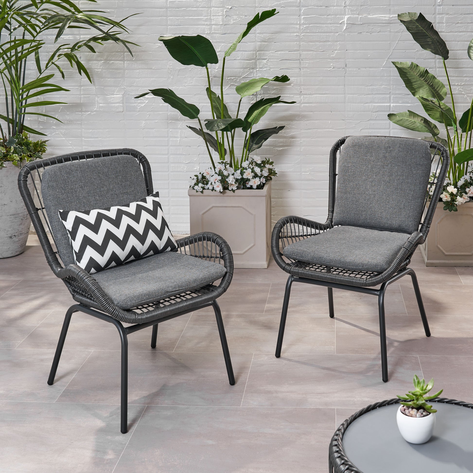 Two dark grey woven wicker patio chairs with cushions one with a chevron pillow