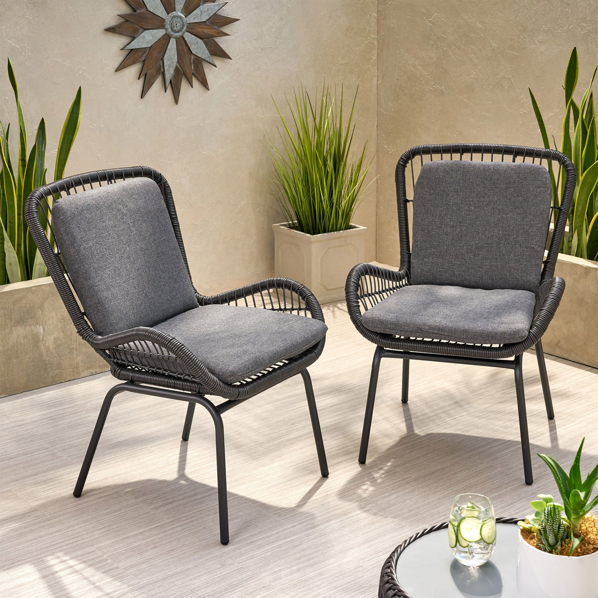 Two dark grey wicker outdoor chairs with plush grey cushions on a patio setting