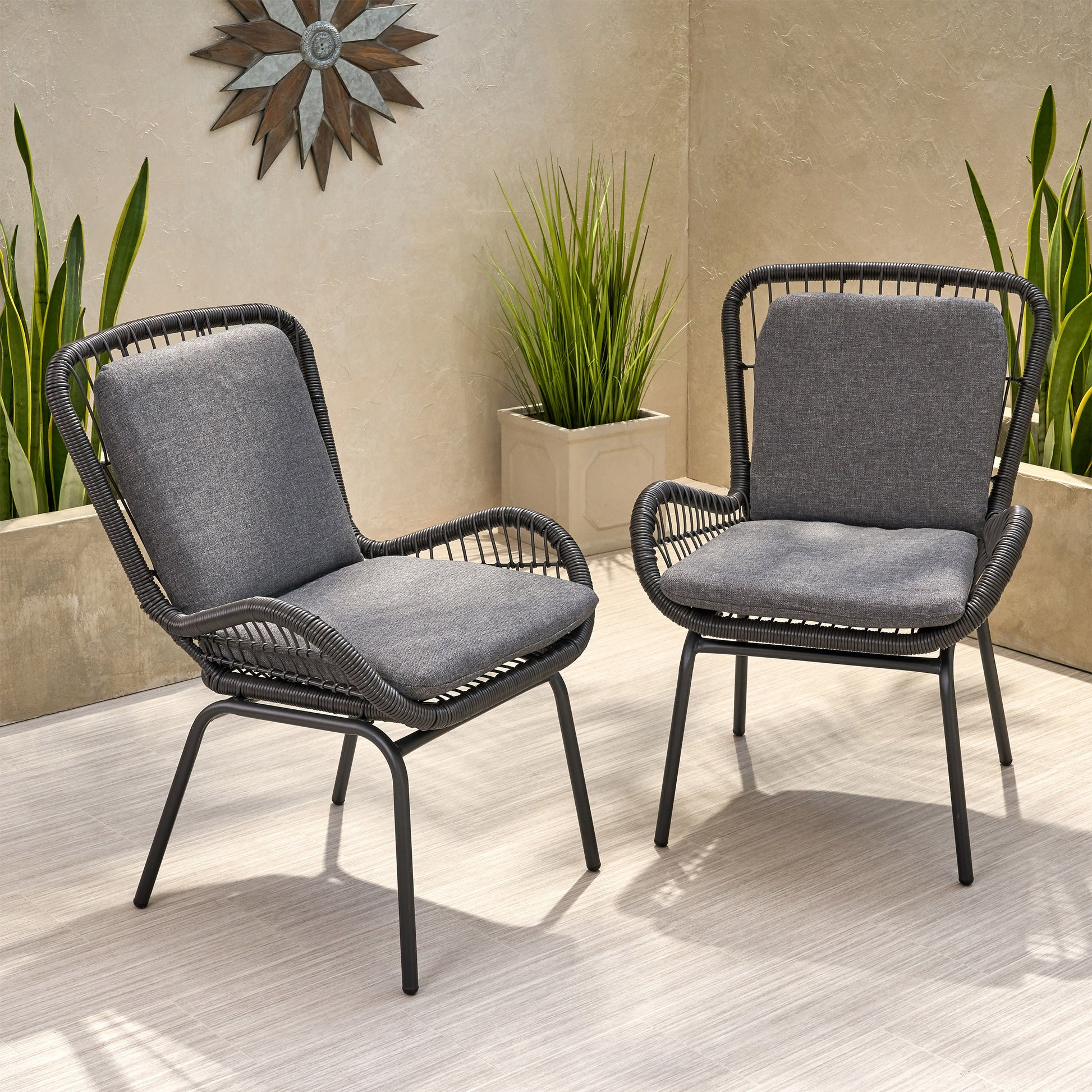 Two grey rattan outdoor accent chairs with comfortable cushions on a tiled patio