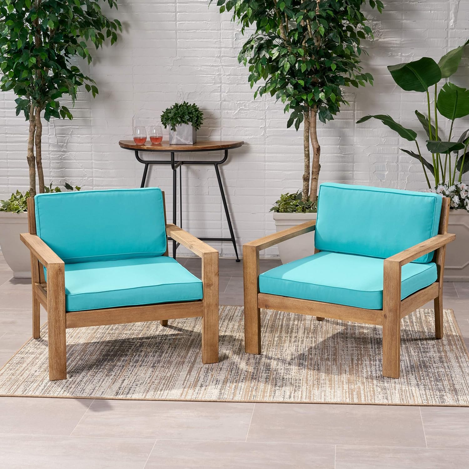 Two wooden patio chairs with vibrant teal cushions on a striped outdoor rug